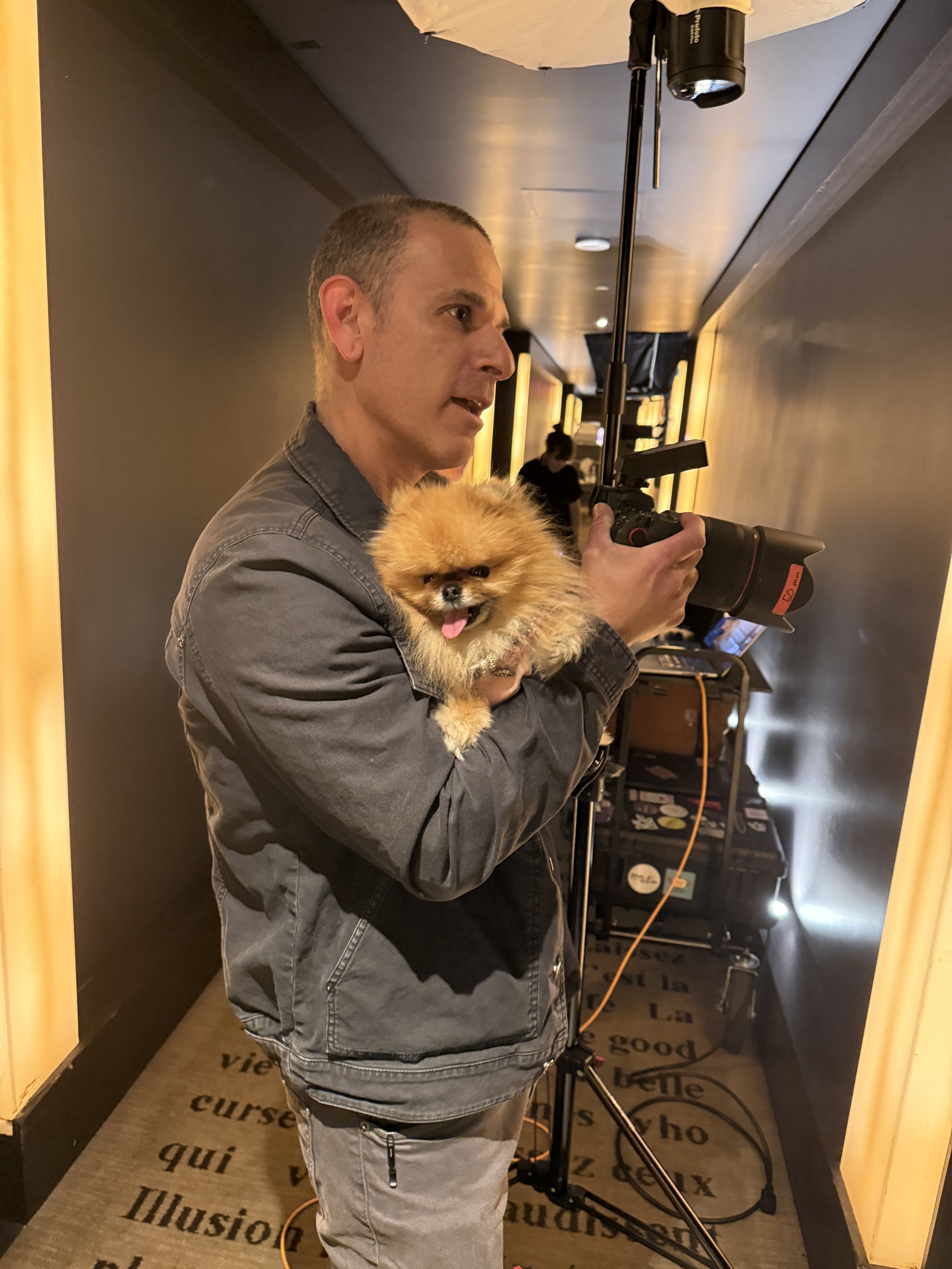 Michael Rudin photographing Lisa Vanderpump on set in a mock hotel suite, holding her Pomeranian while working the camera
