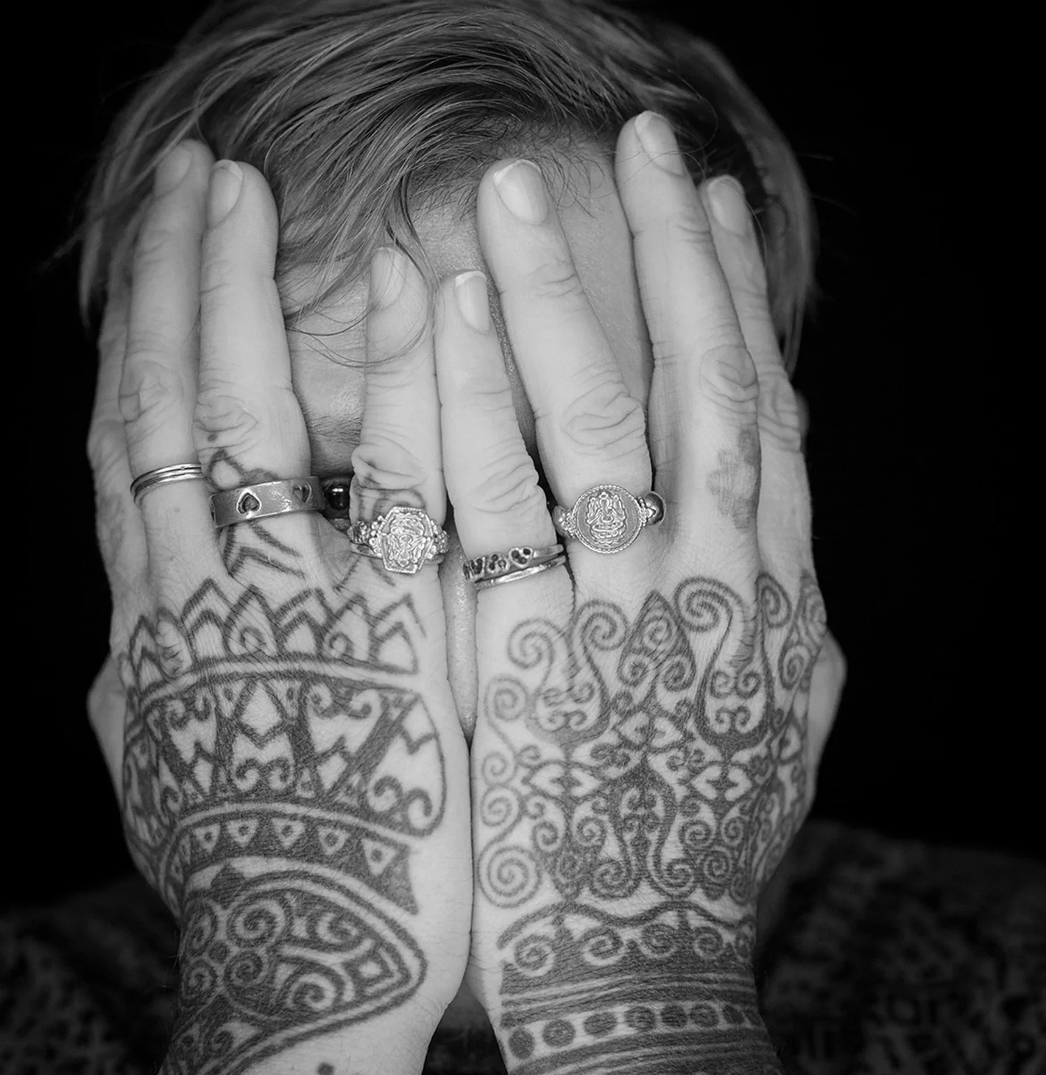 Black and white close-up of tattooed hands covering a face, personal portrait by Michael Rudin