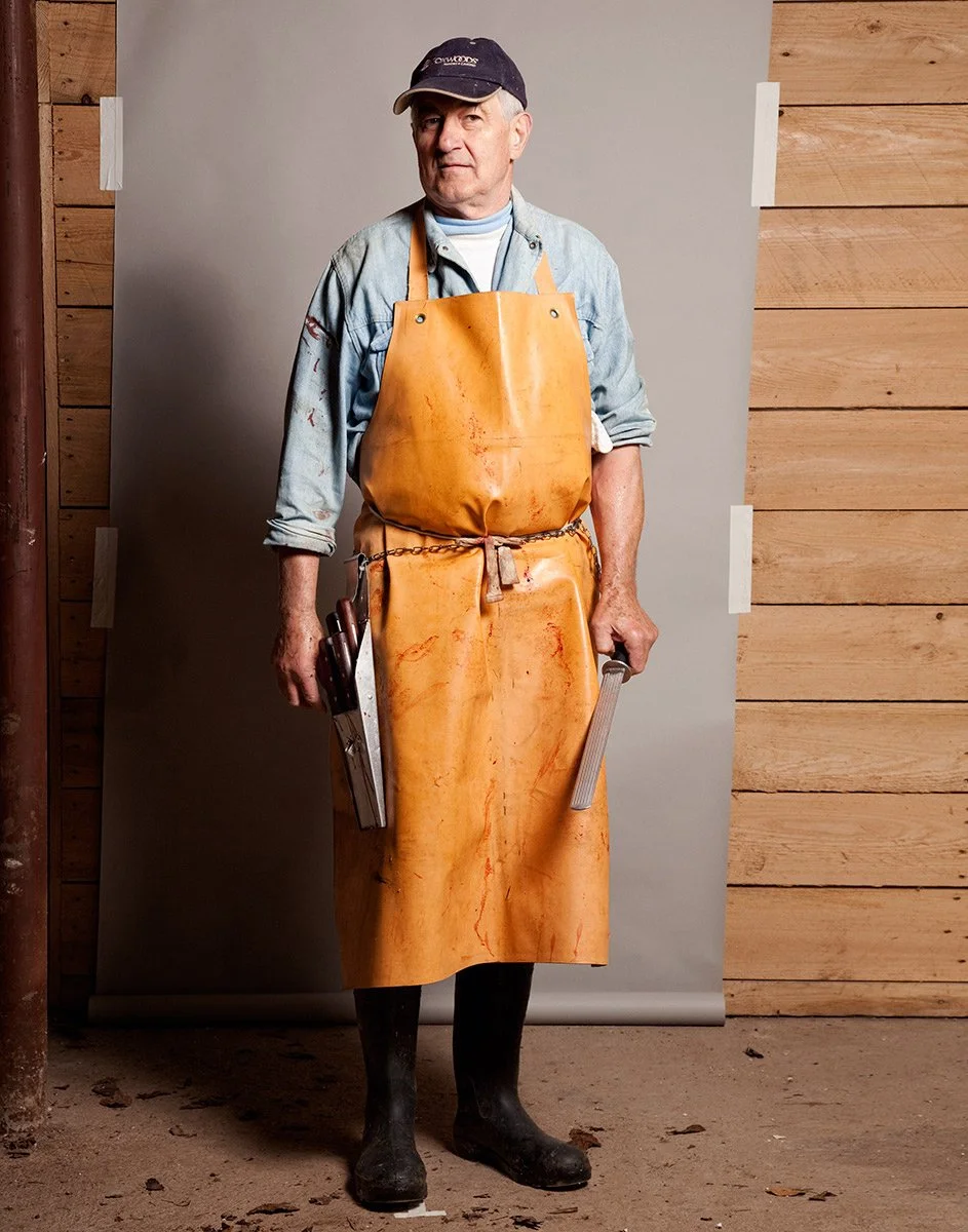 Butcher in a leather apron holding knives, editorial portrait by Michael Rudin