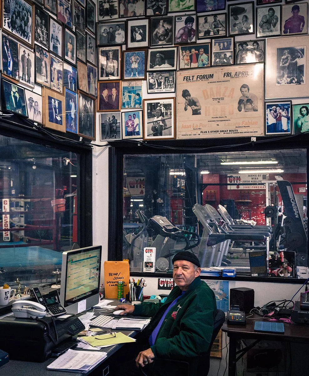 Man seated at a desk inside the historic Gleason's Gym boxing club, editorial portrait by Michael Rudin