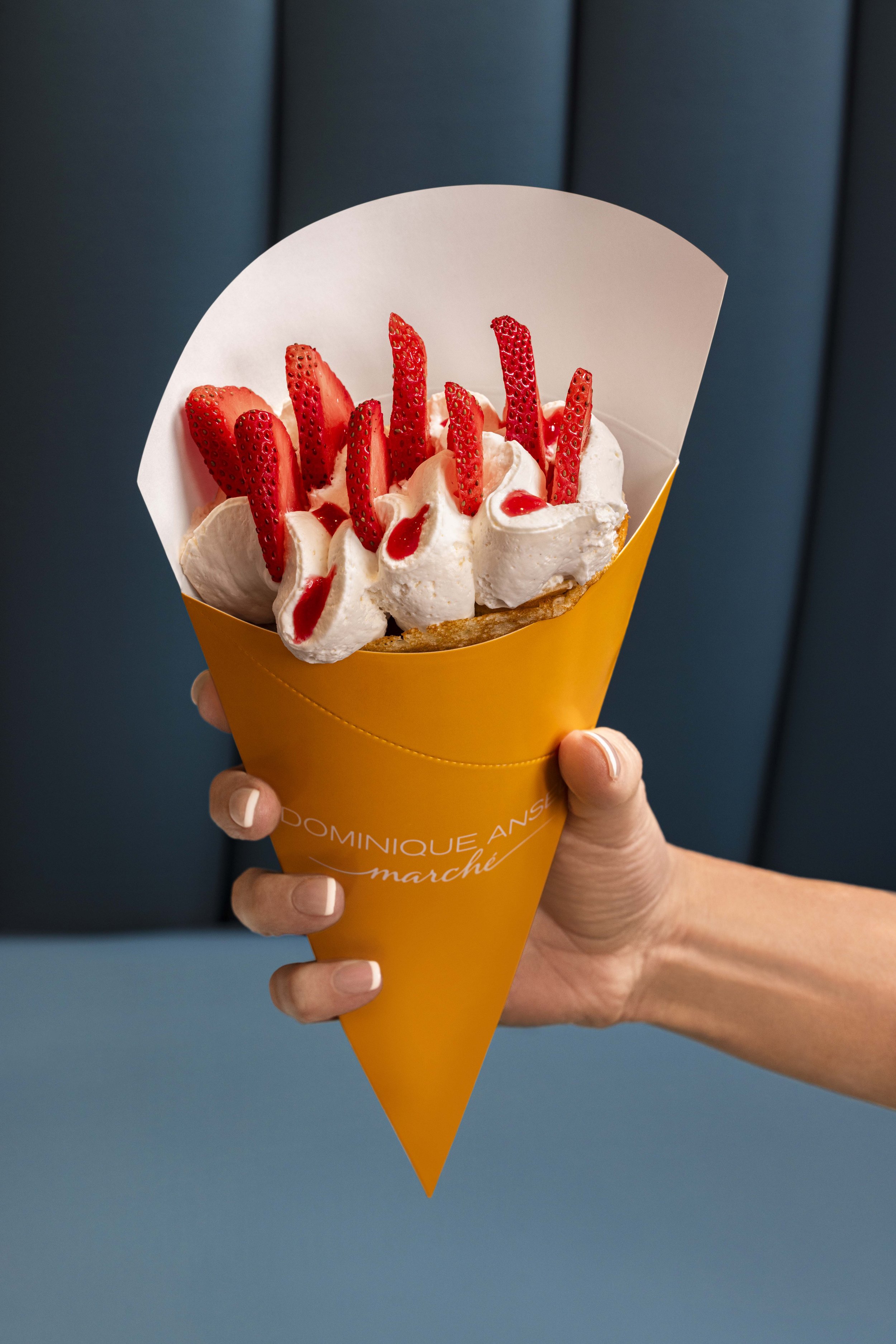Strawberry crepe cone with whipped cream, held in hand