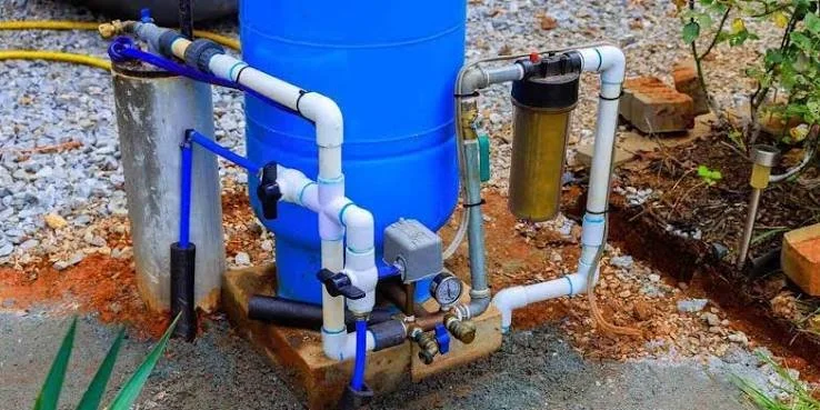 A water filtration system installed outdoors with pipes, a blue water tank, a filter, and valves.