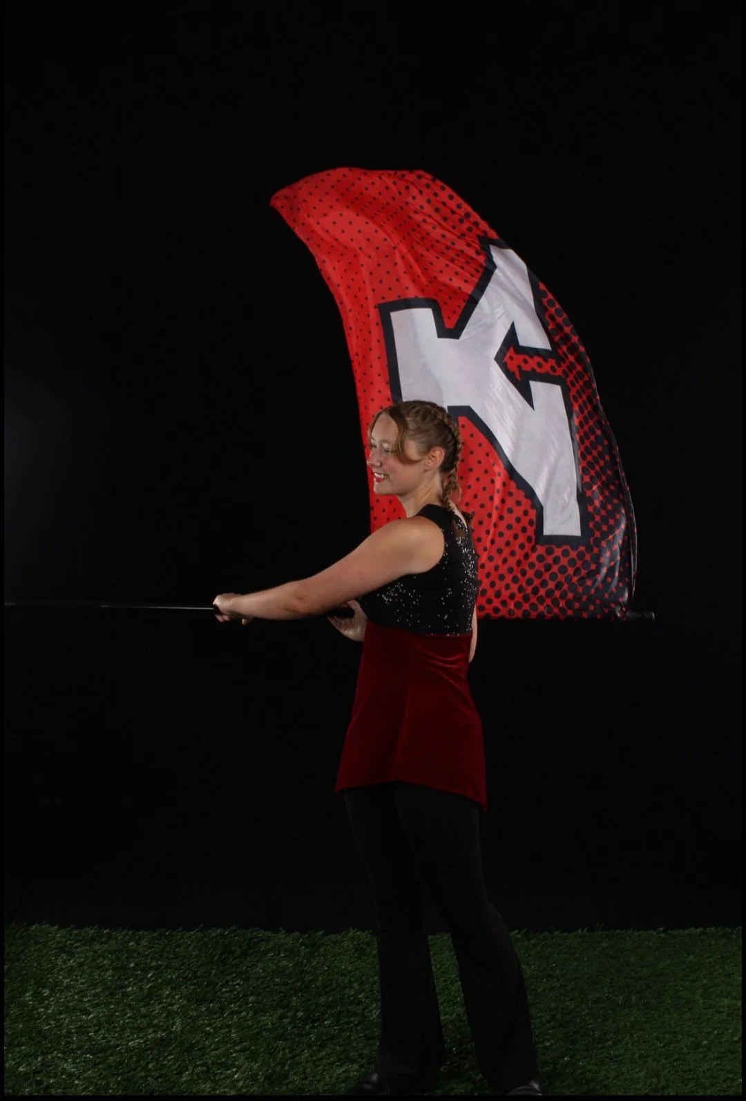 A woman smiling while spinning a large red and black flag with a 'Y' on it, against a black background.