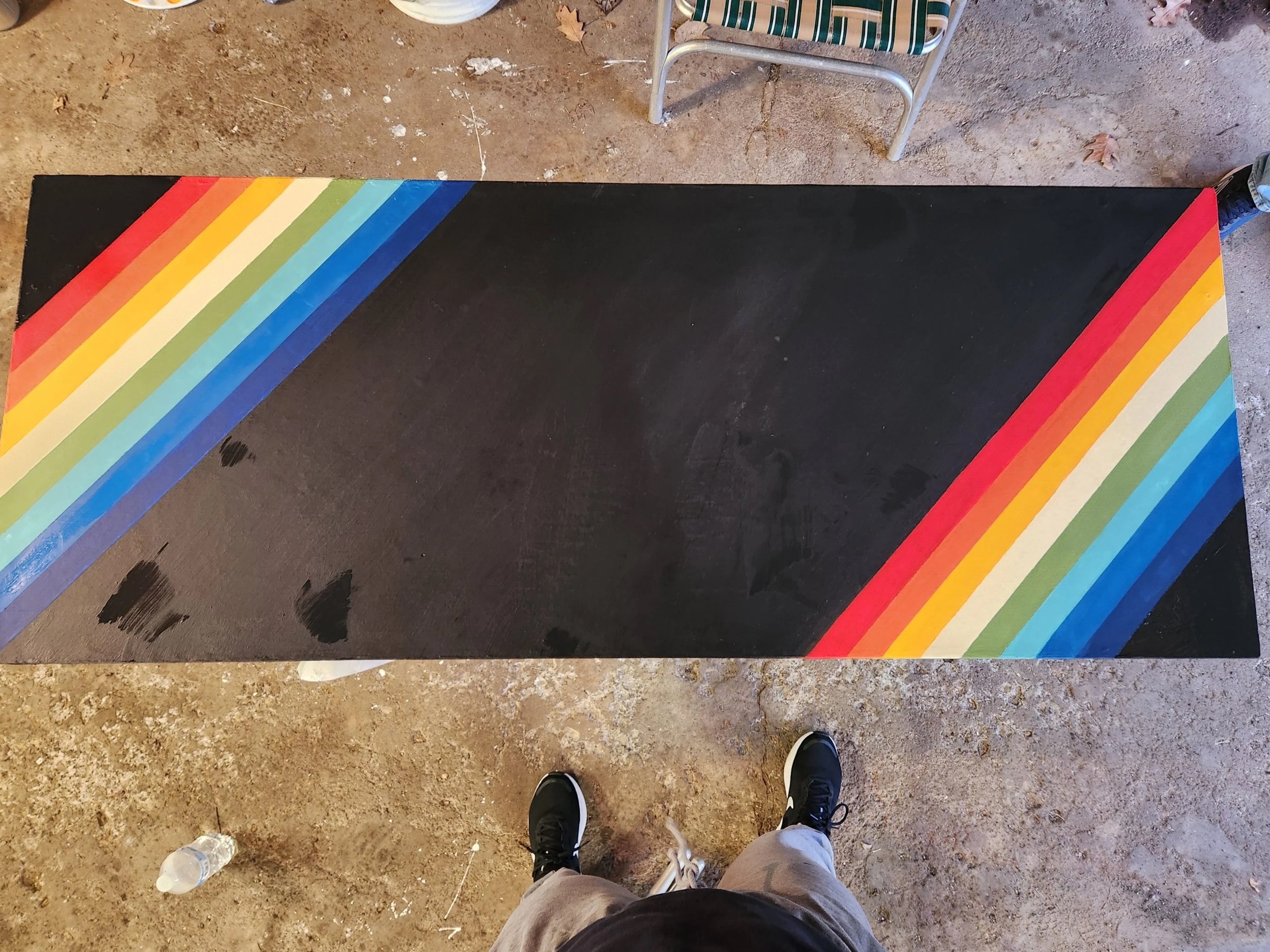 Top-down view of a person standing on a dirt ground, with retro-colored stripes painted on a desk in front.