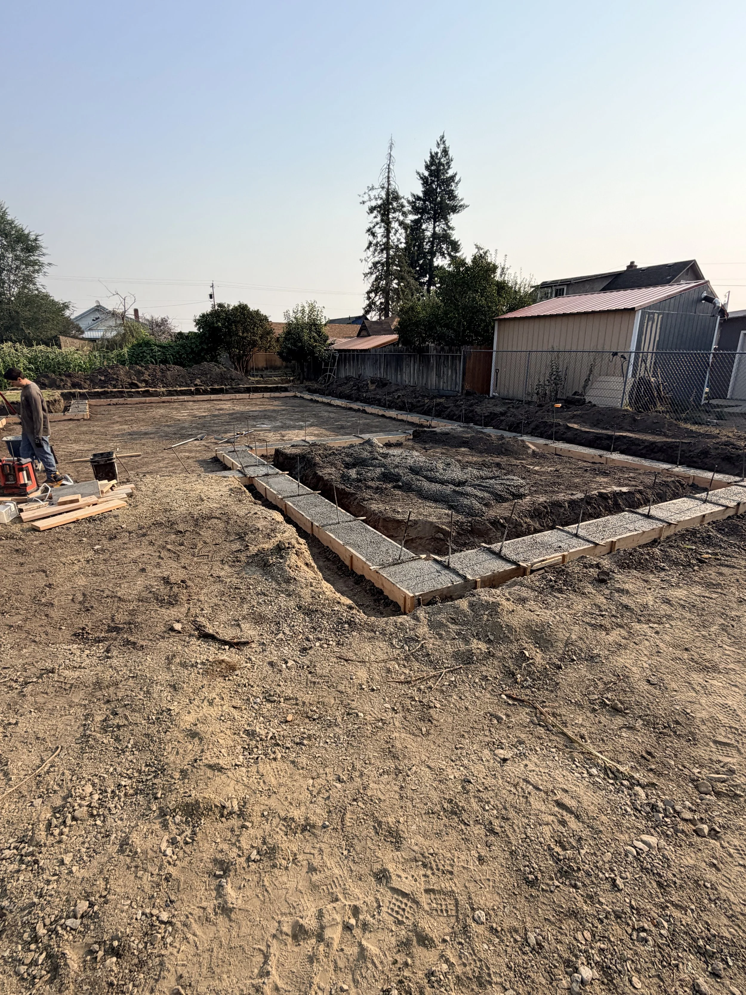 A construction site with the foundation being prepared for building, showing dirt, gravel, and concrete blocks with a person working on the site.