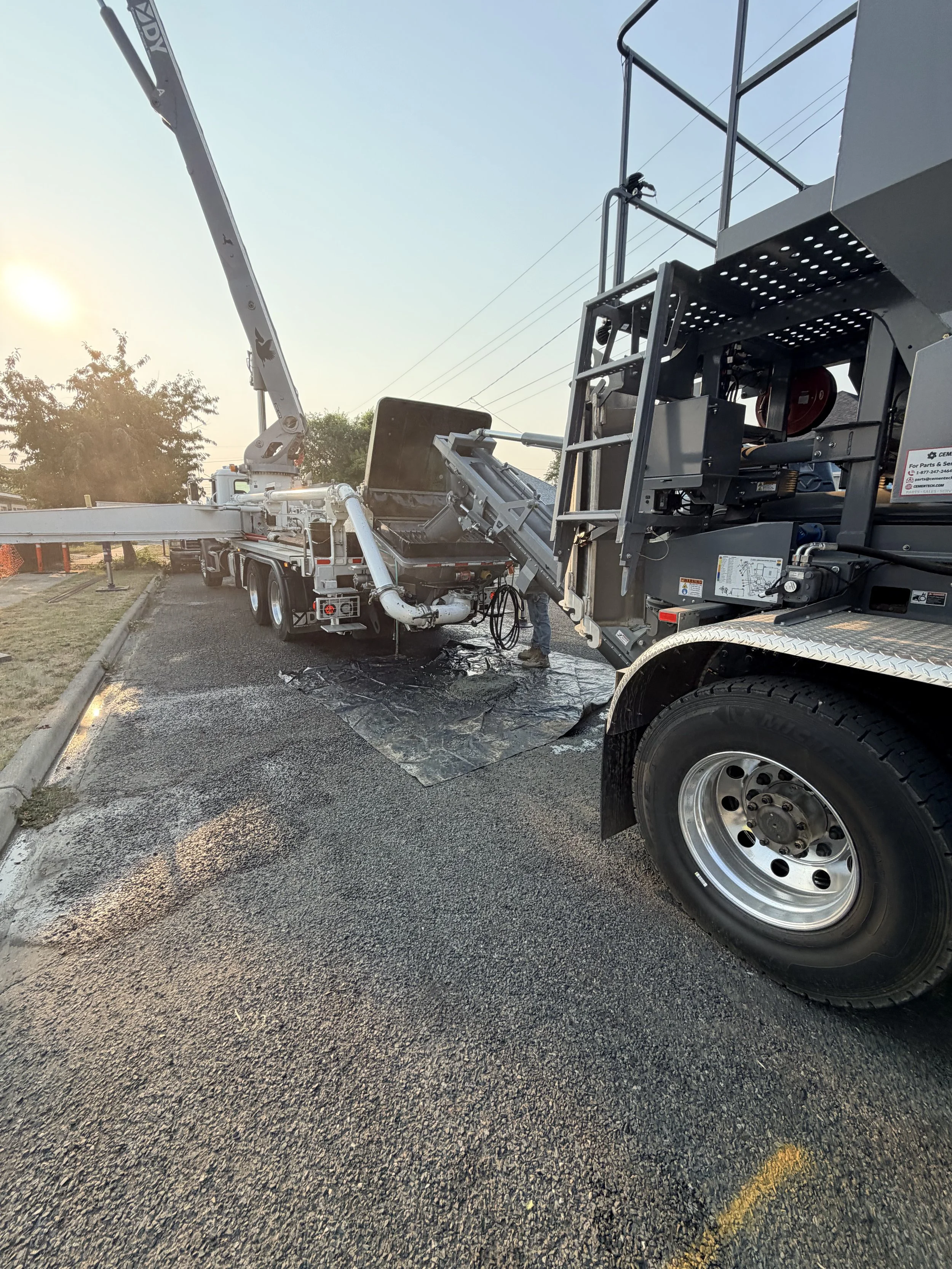 A concrete pump truck (Cemen Tech C60) with a long boom extended, parked on a paved surface during sunset, with trees and power lines in the background.