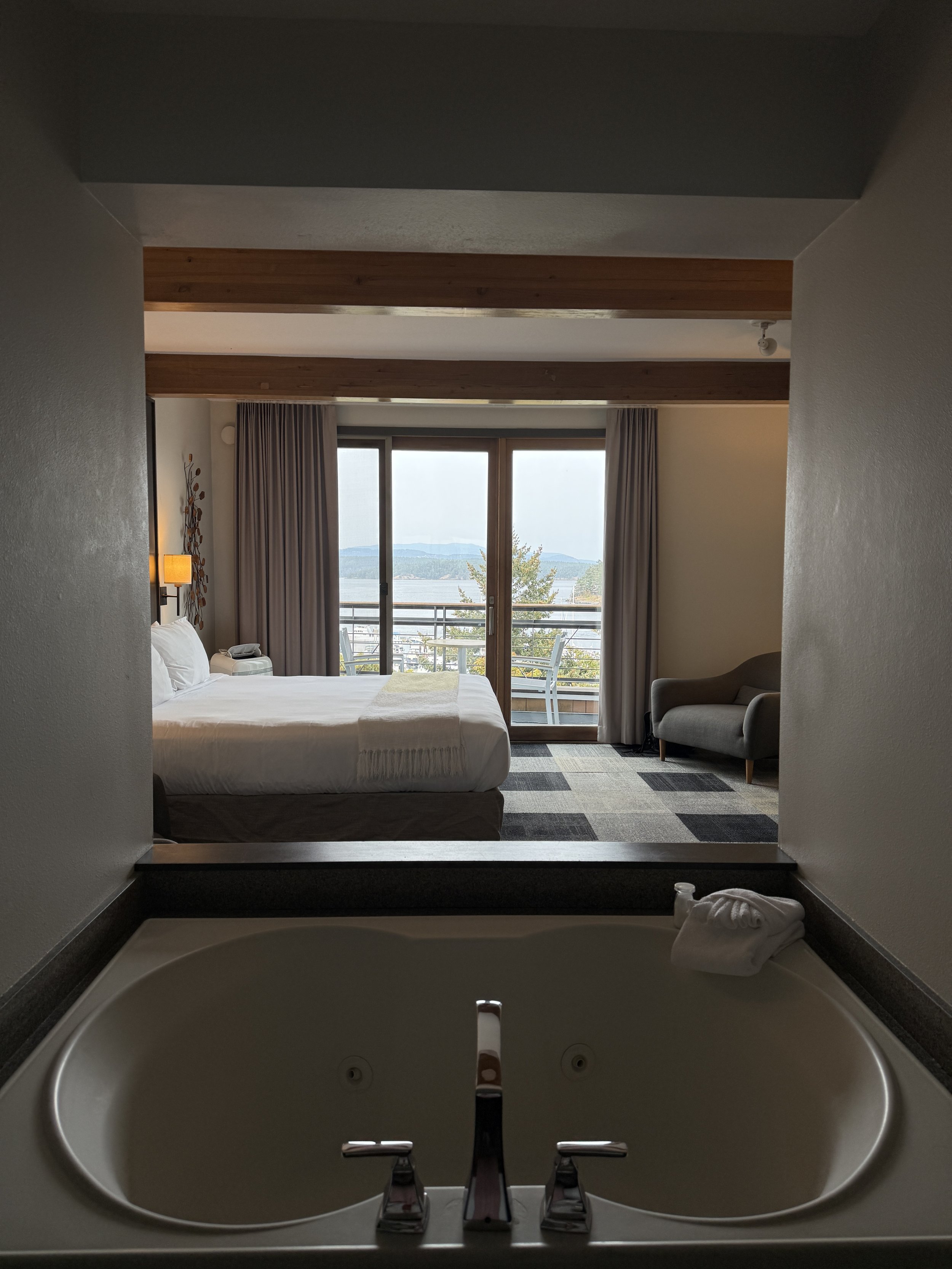 Sunken bathtub in front of a bed with open blinds and a view of water and mountains