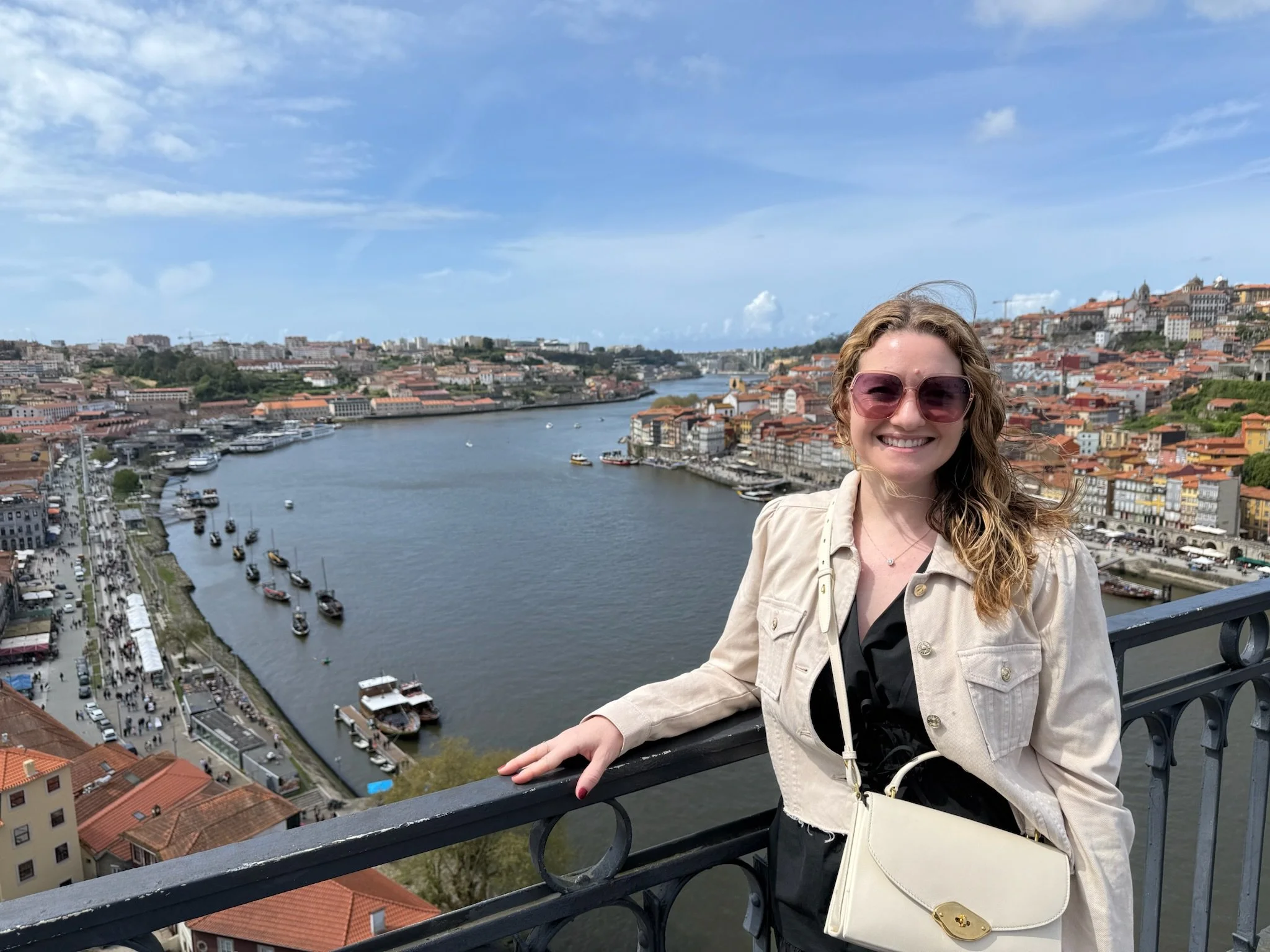 A woman smiling and standing on a bridge overlooking Porto