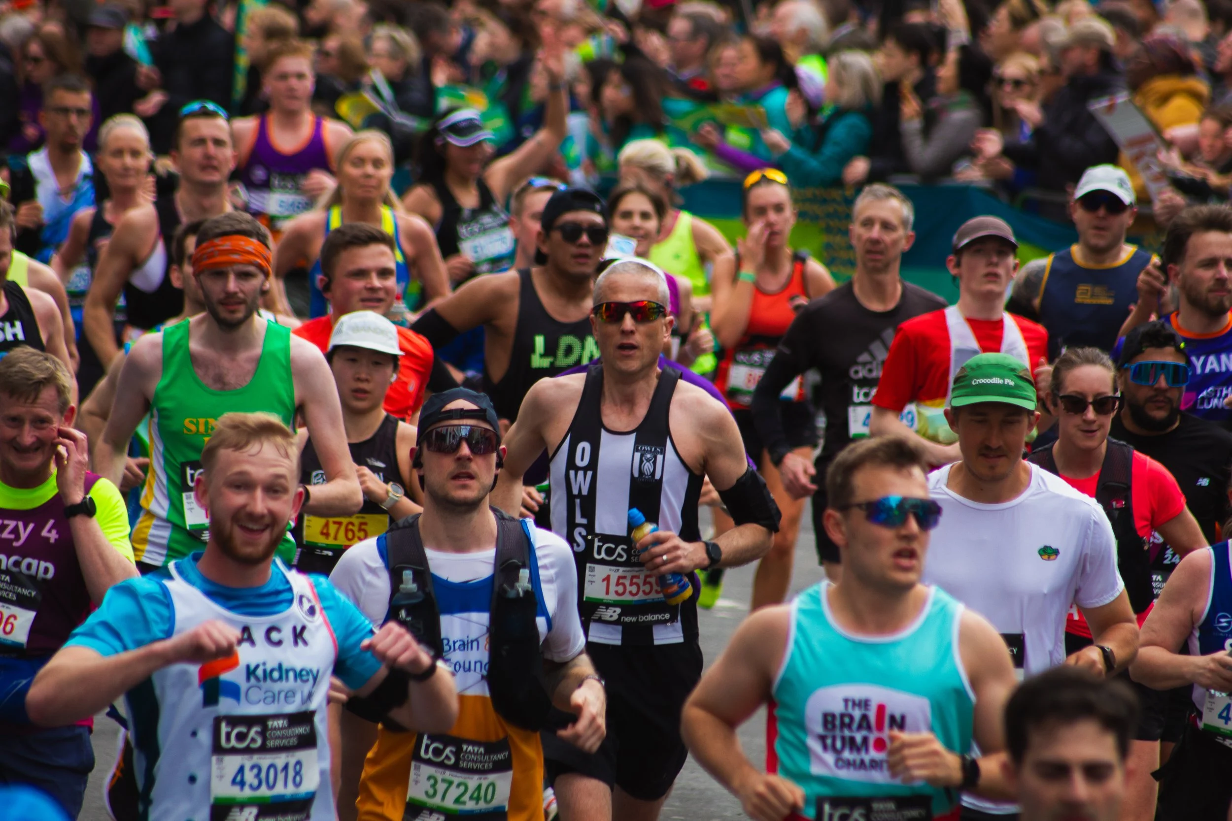 A large group of marathon runners participating in a race outdoors, many wearing sport attire and sunglasses.