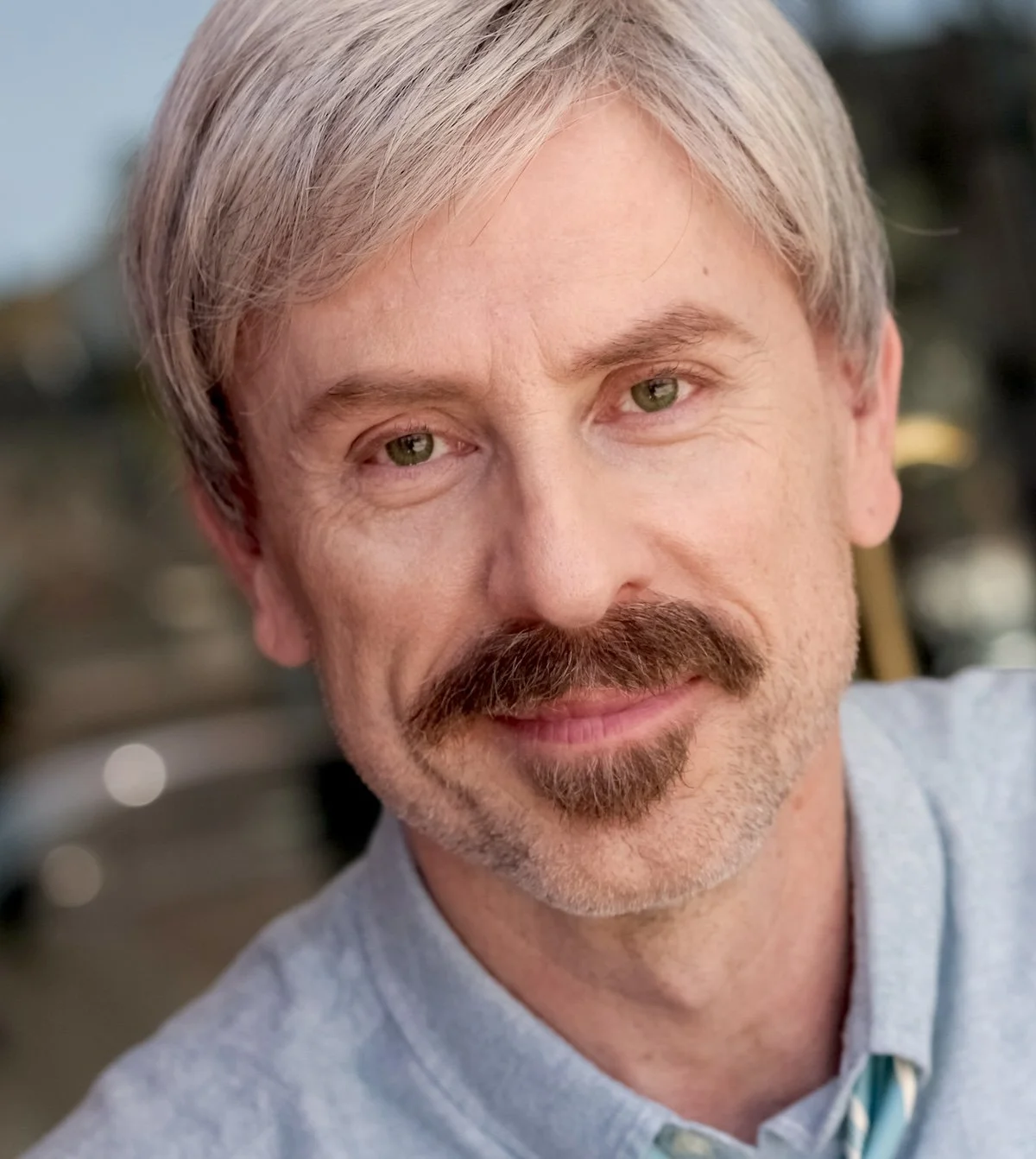 Close-up of Robert Ackerman Moss with gray hair and a mustache, smiling softly outdoors.