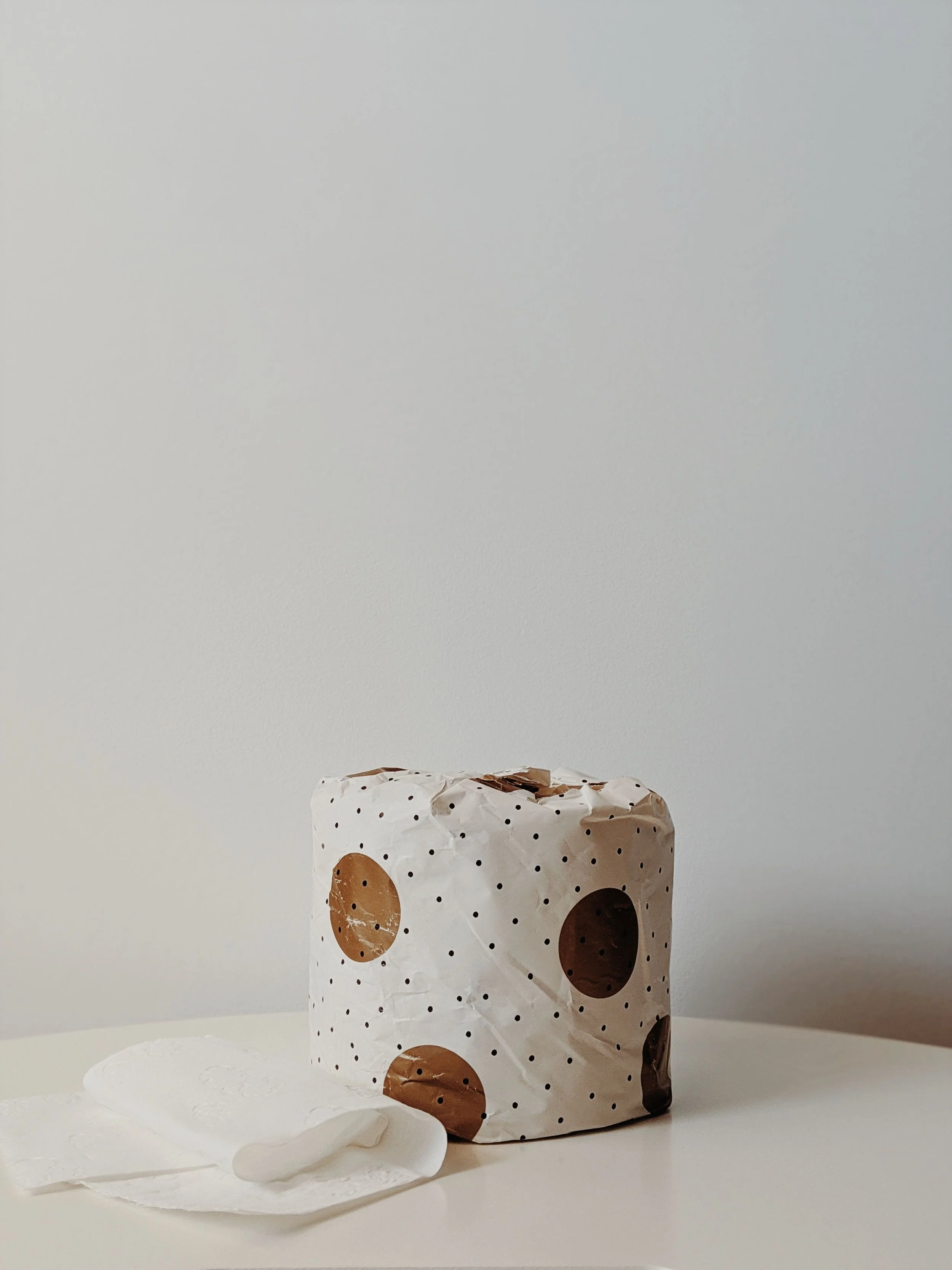 A coffee cup wrapped in white paper with brown and black polka dots, partially covered by white tissues on a white surface against a neutral background.