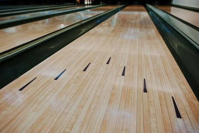 Bowling alley lane with wooden flooring and gutters on either side.