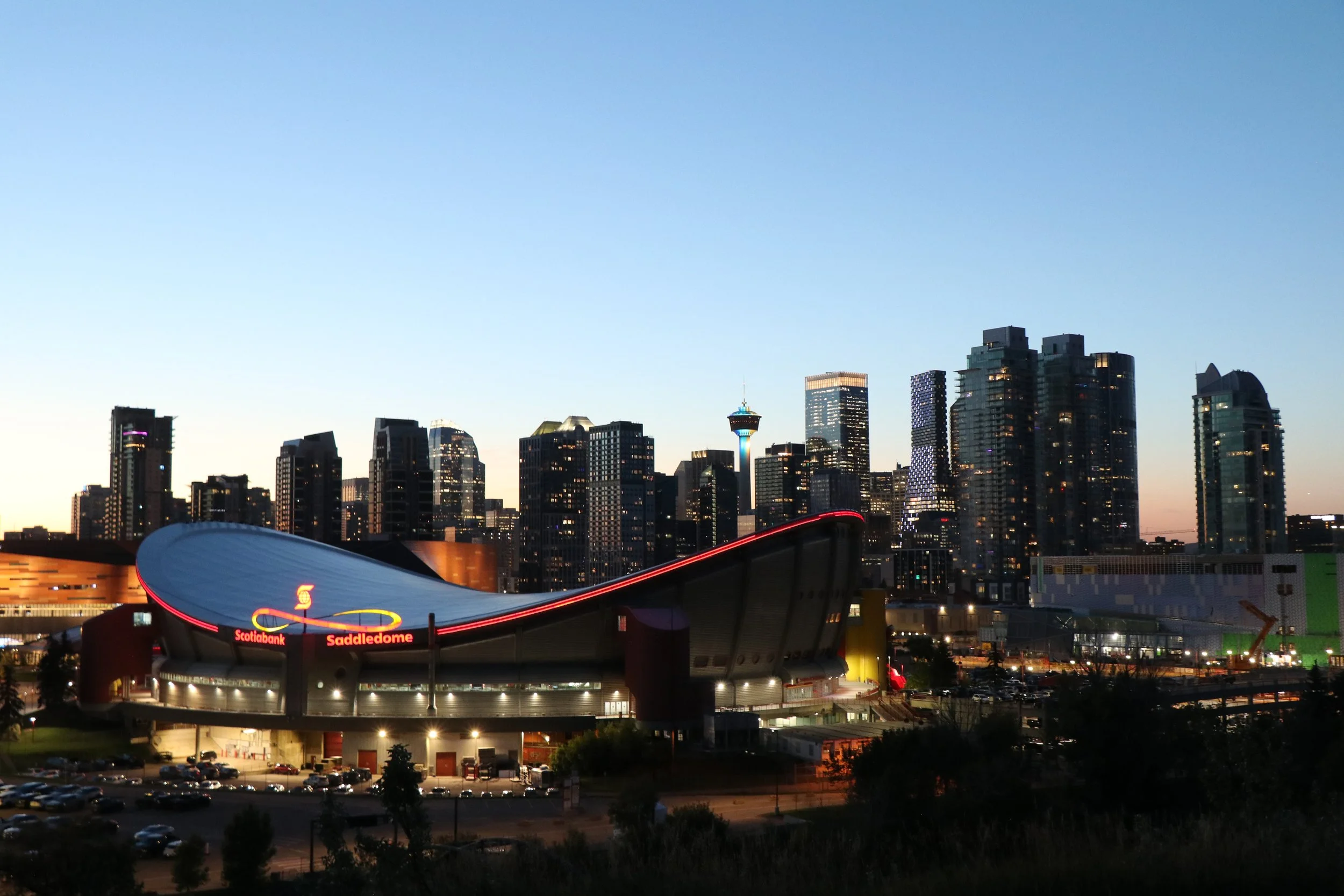 Seattle skyline at dusk with illuminated buildings and the Scotiabank Saddledome in the foreground.