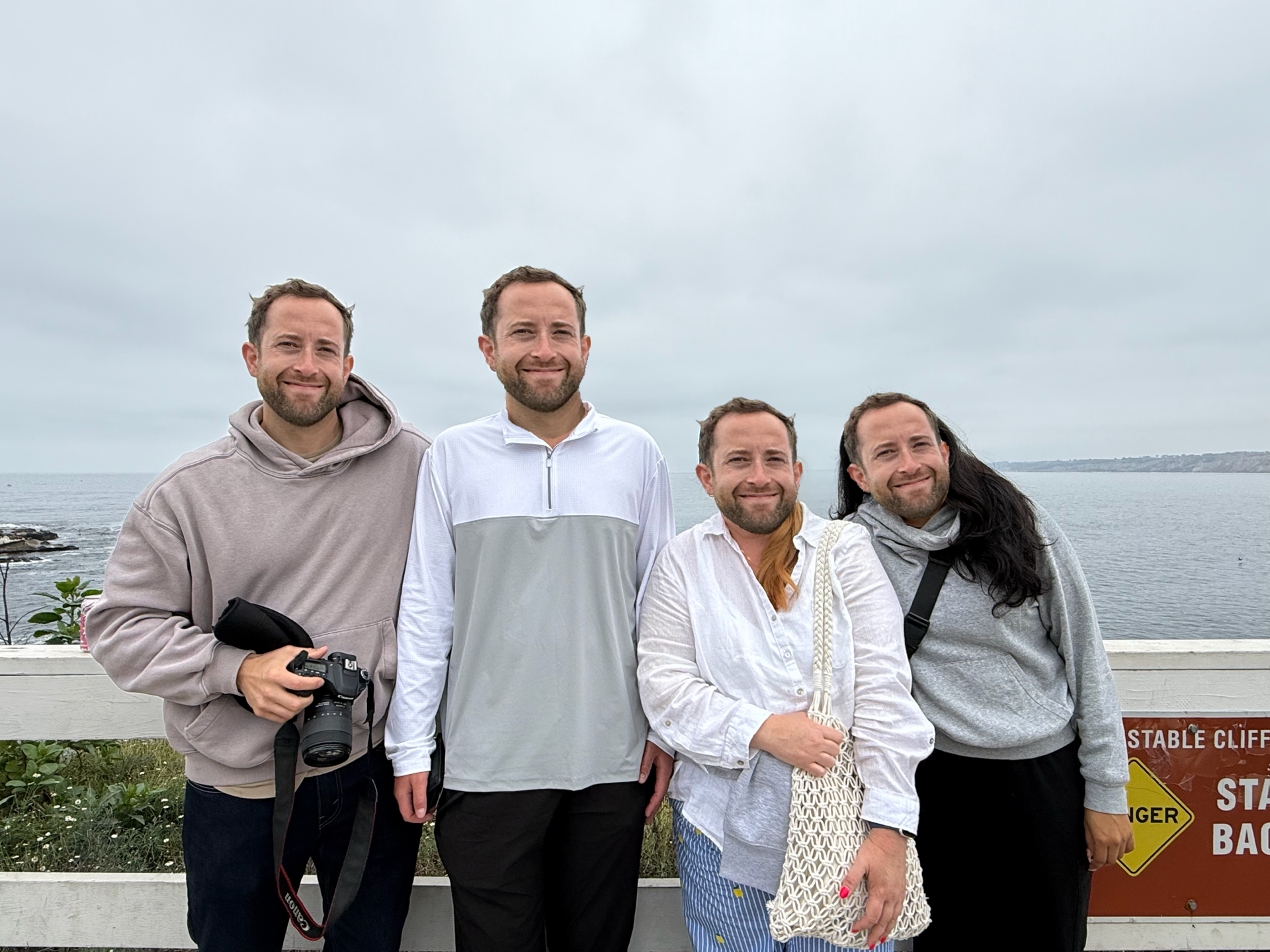 Group of five people standing outdoors near water on cloudy day, smiling for the camera.
