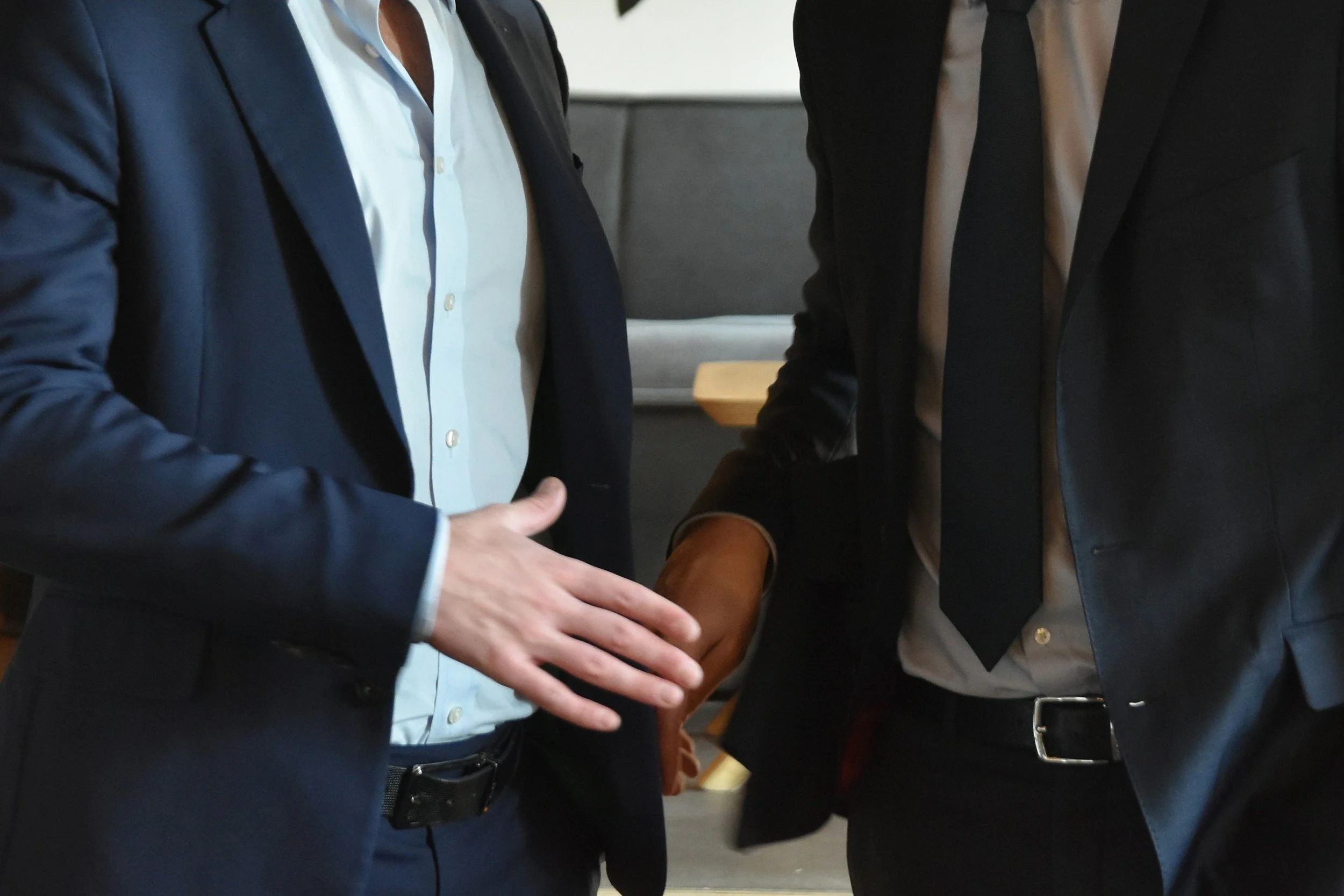 Two people in business attire shaking hands in an office or conference room setting.
