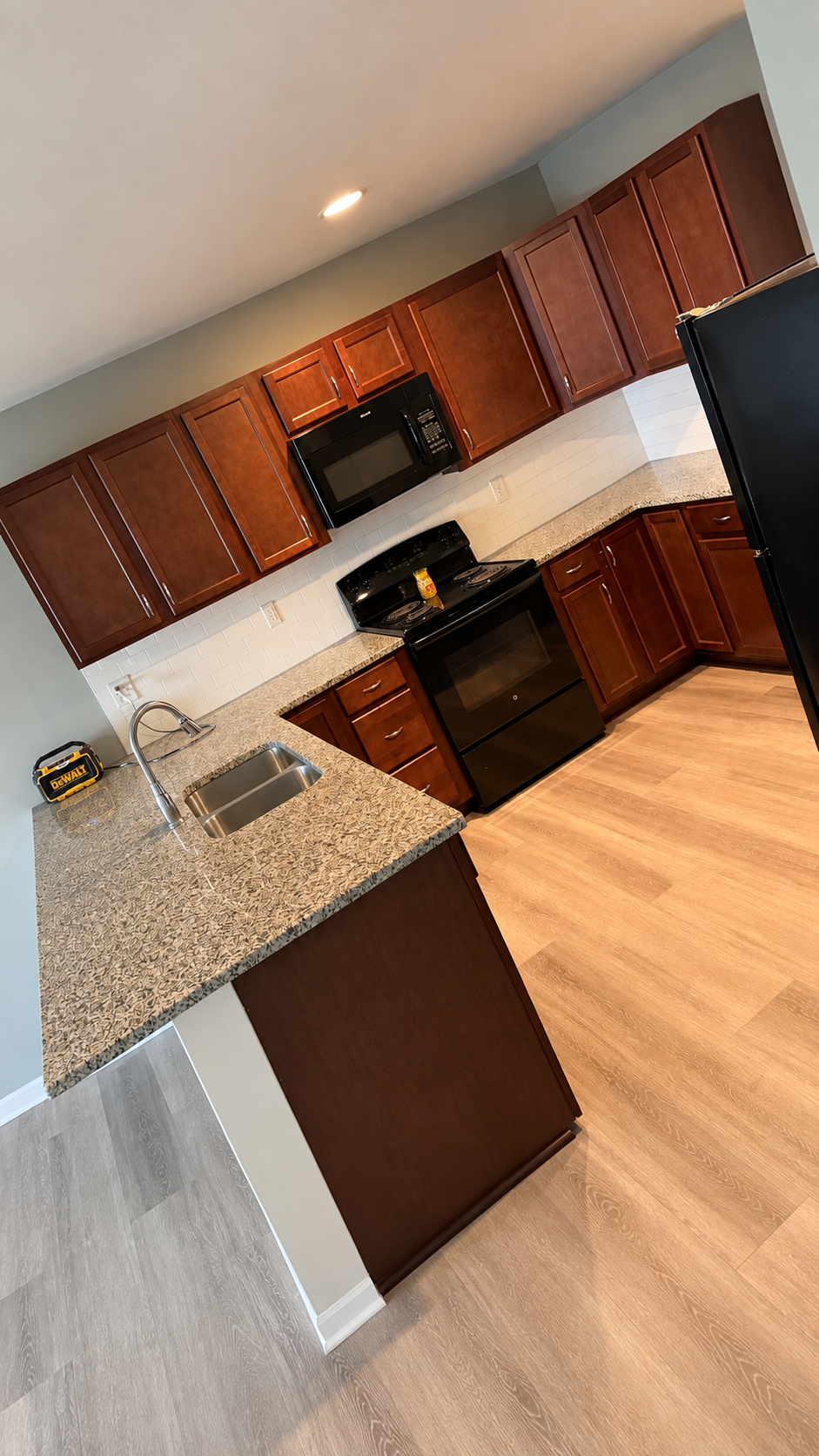 Kitchen with dark wood cabinets, black appliances, granite countertops, light wood flooring, and a small black toolbox on the counter.