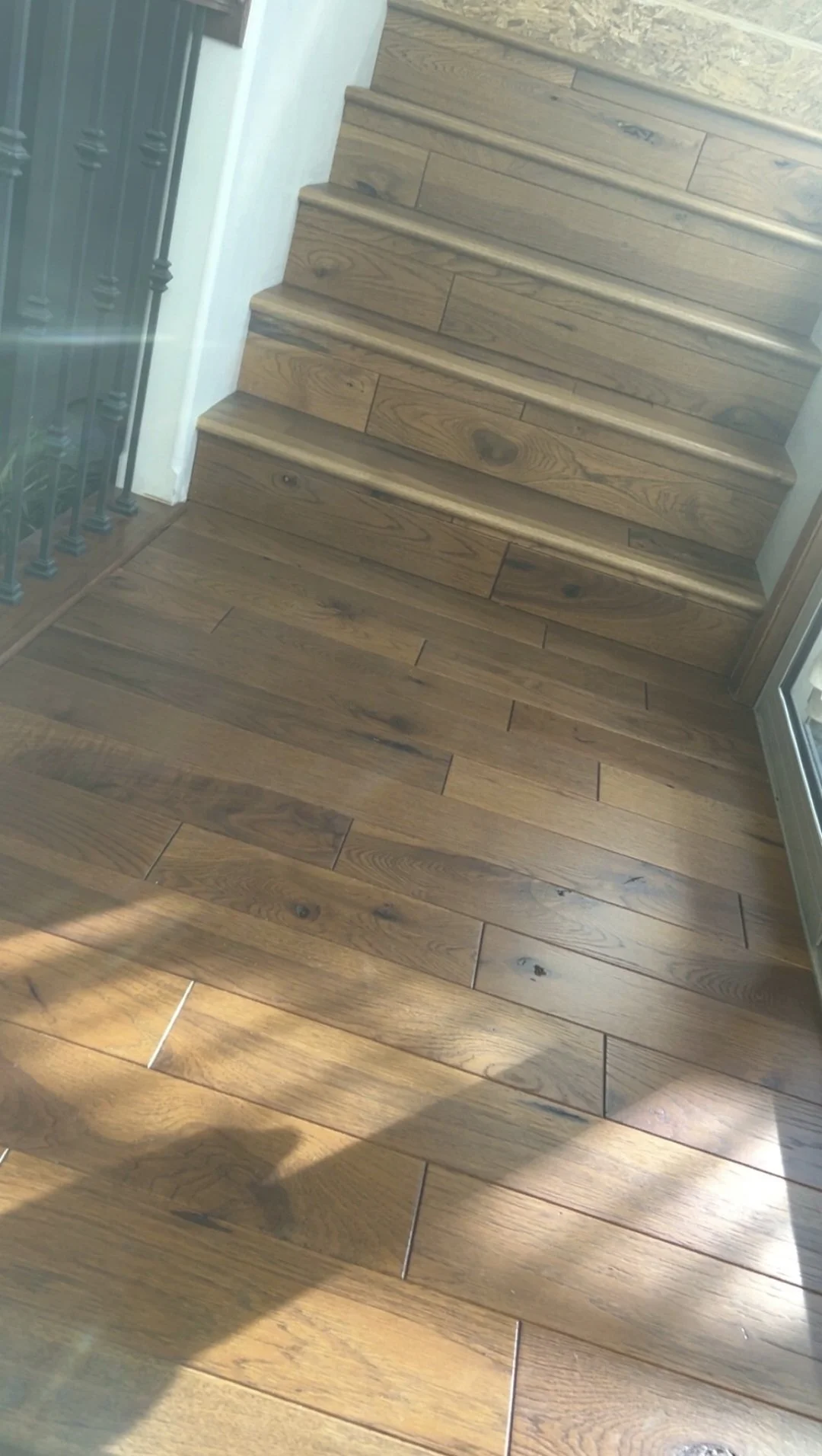 Wooden staircase with matching wood flooring at the bottom, next to a white wall and a glass window.