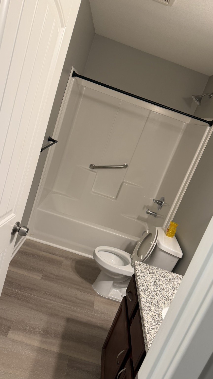 Bathroom with grey walls, a shower stall with a grab bar, a toilet, and a dark wood vanity with a granite countertop.