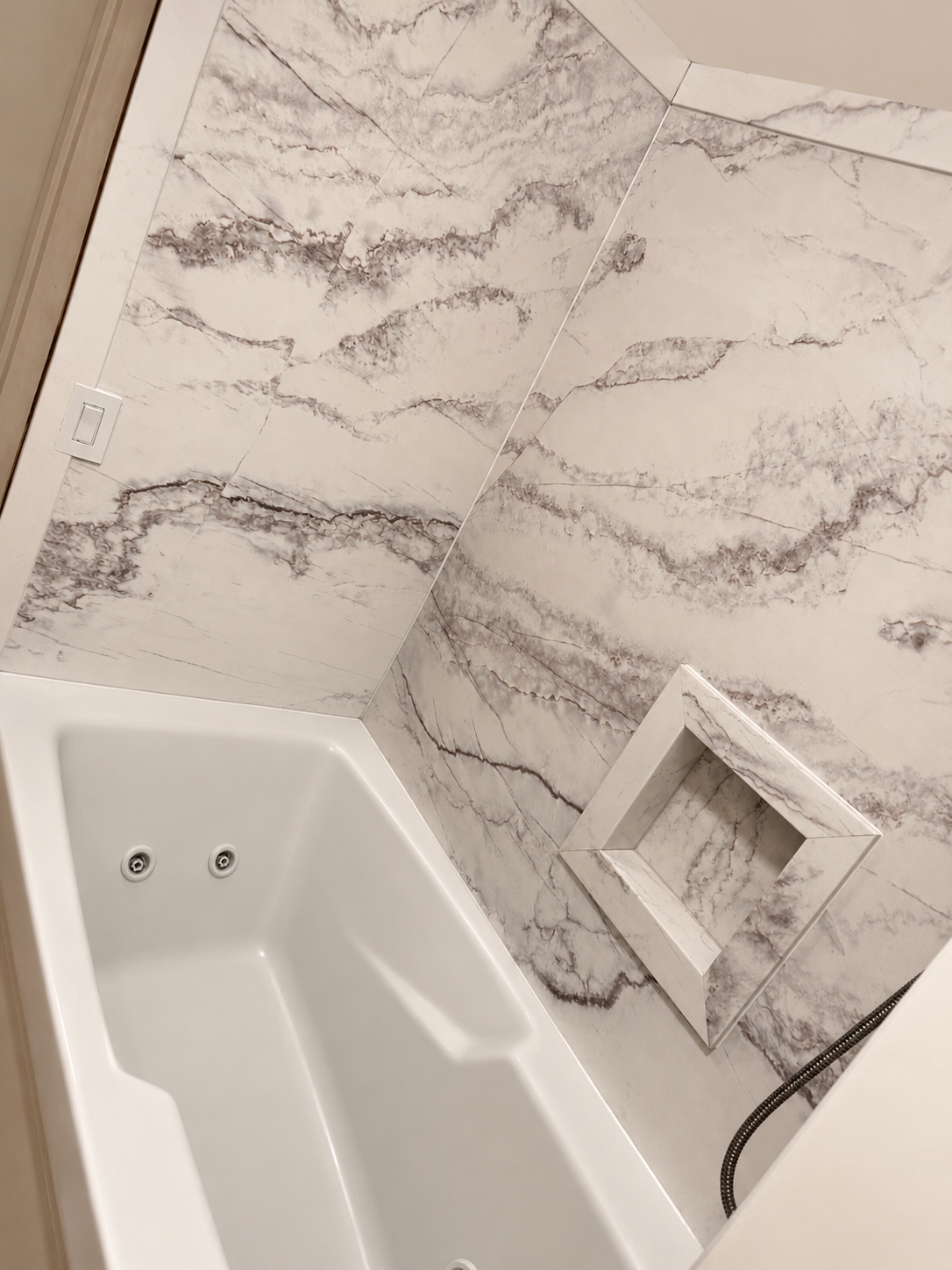 Close-up of a bathtub with jets, surrounded by marble tiles, including a built-in marble shelf.