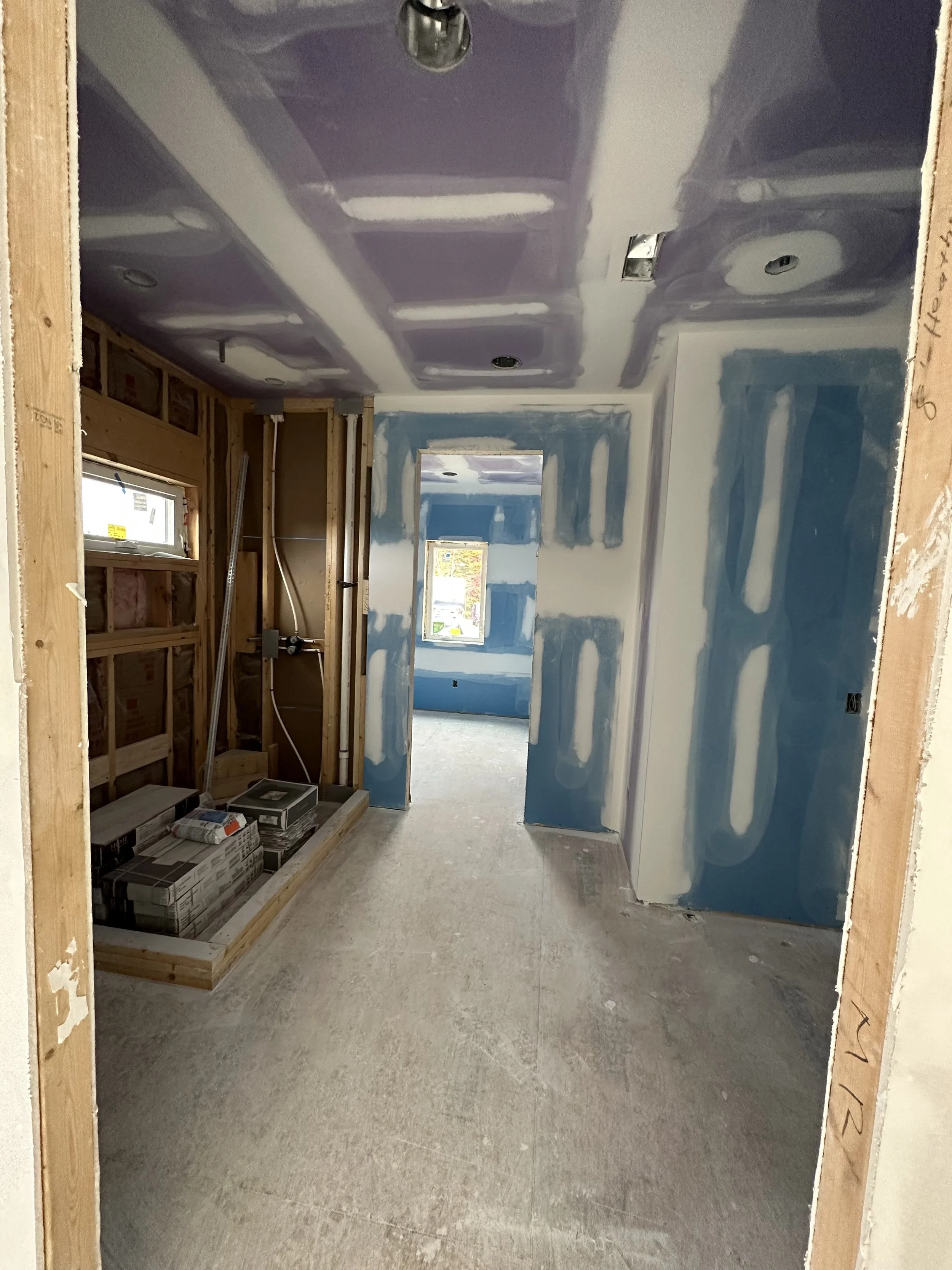 Interior of a house under renovation, showing drywall installation with visible seams, electrical wiring, and boxes, with unfinished flooring and framing in doorways.