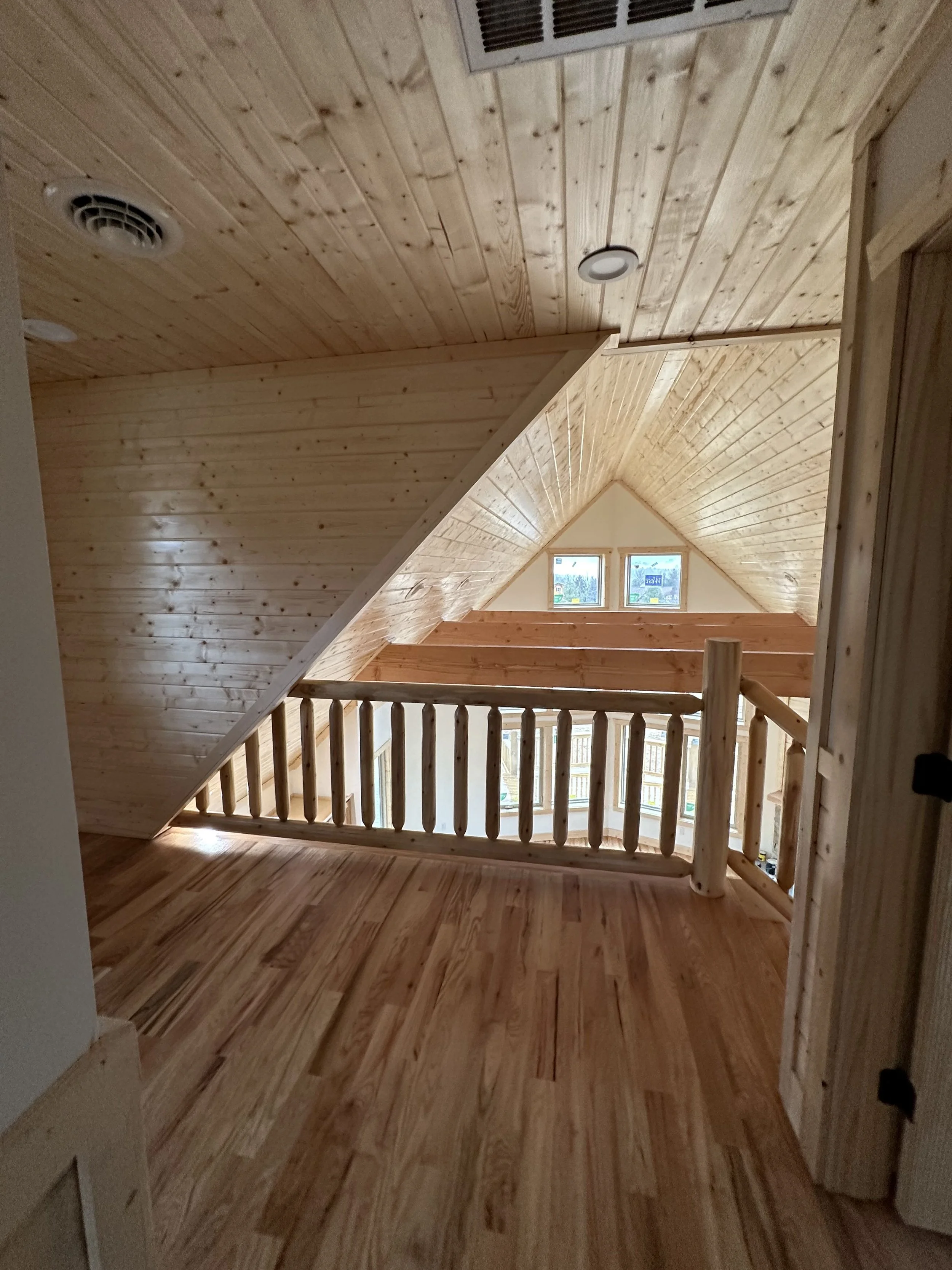 Interior view of a wooden attic space with ceiling and floor made of natural wood planks, a small window, and a wooden railing.
