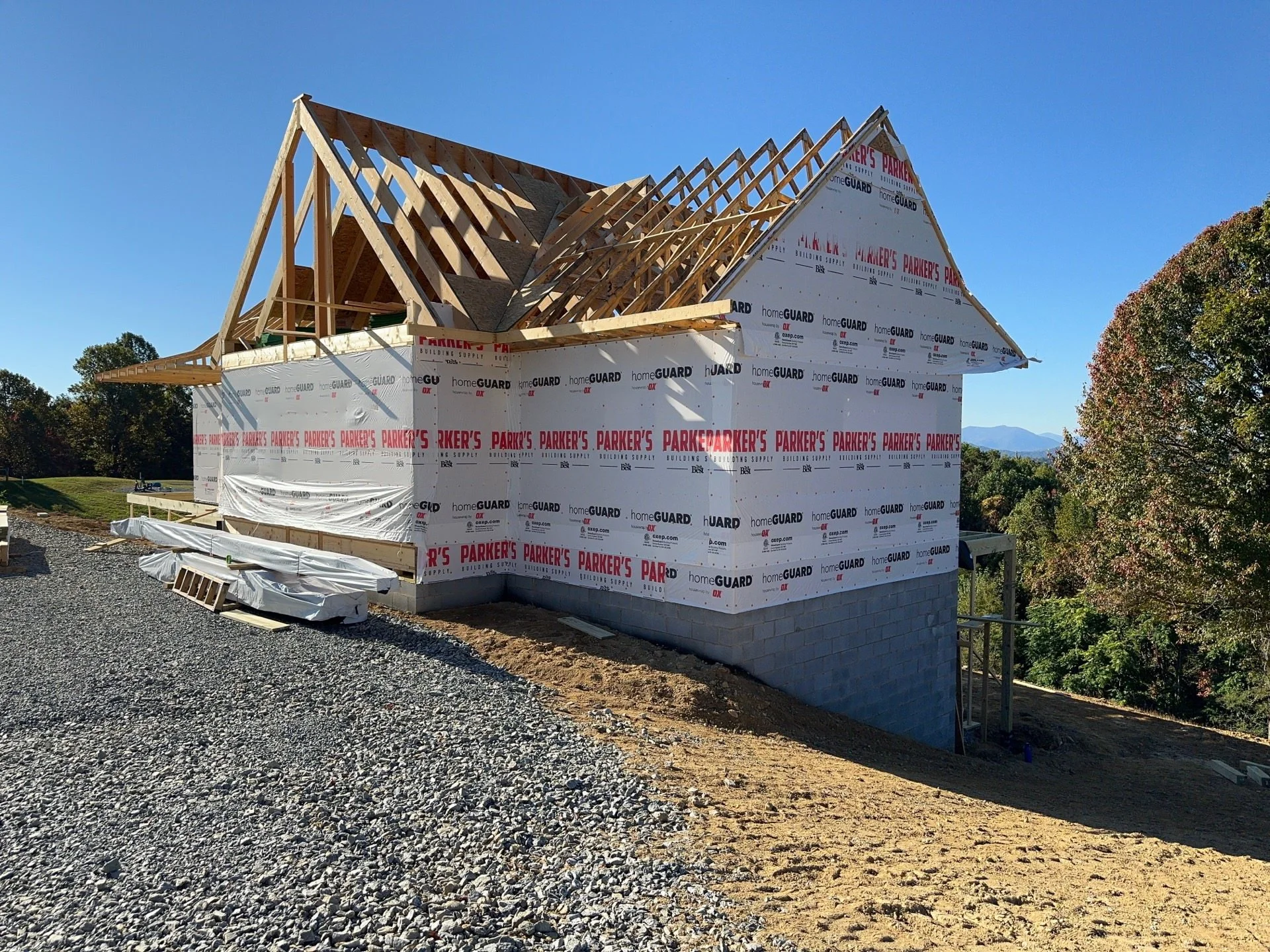 A house under construction showing wooden roof trusses and partially installed exterior wall sheathing with building material branding.