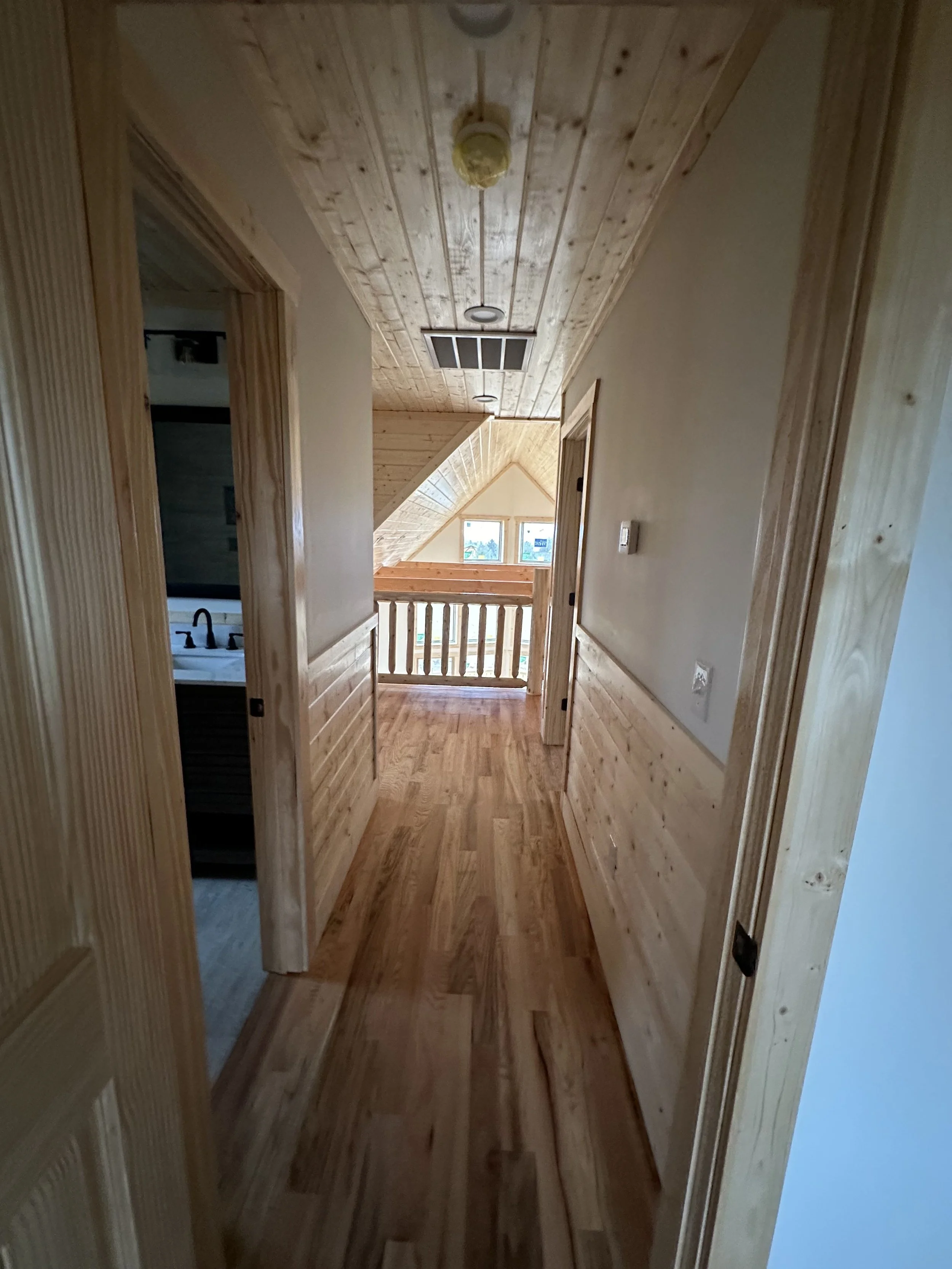 A hallway with wood paneling on the walls and ceiling, featuring a skylight window at the end, with two open doorways on either side.