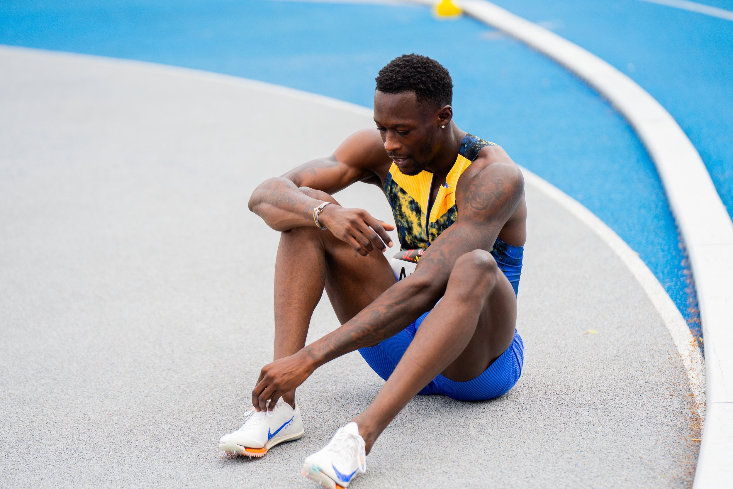 Zwei männliche Läufer sitzen erschöpft am Boden eines Sportplatzes, nachdem sie einen Lauf absolviert haben.
