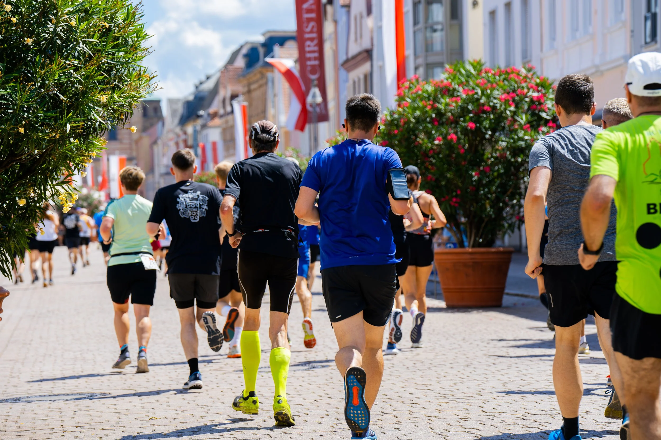 Menschen beim Laufen bei einem Stadtmarathon, mit bunten Kleidung und einem blauen Himmel im Hintergrund.