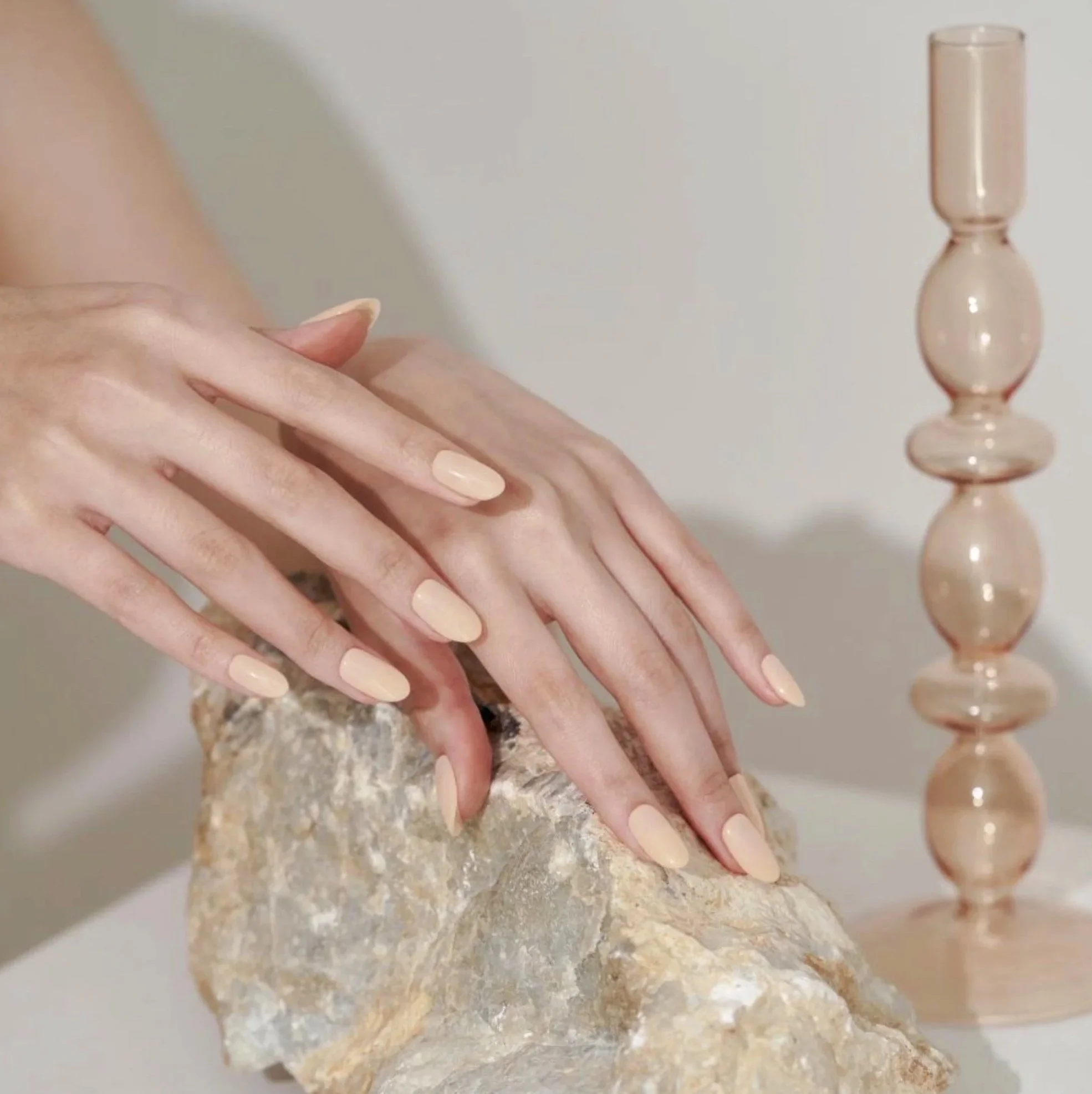 Long nude almond-shaped nails with a glossy finish resting on a textured neutral surface