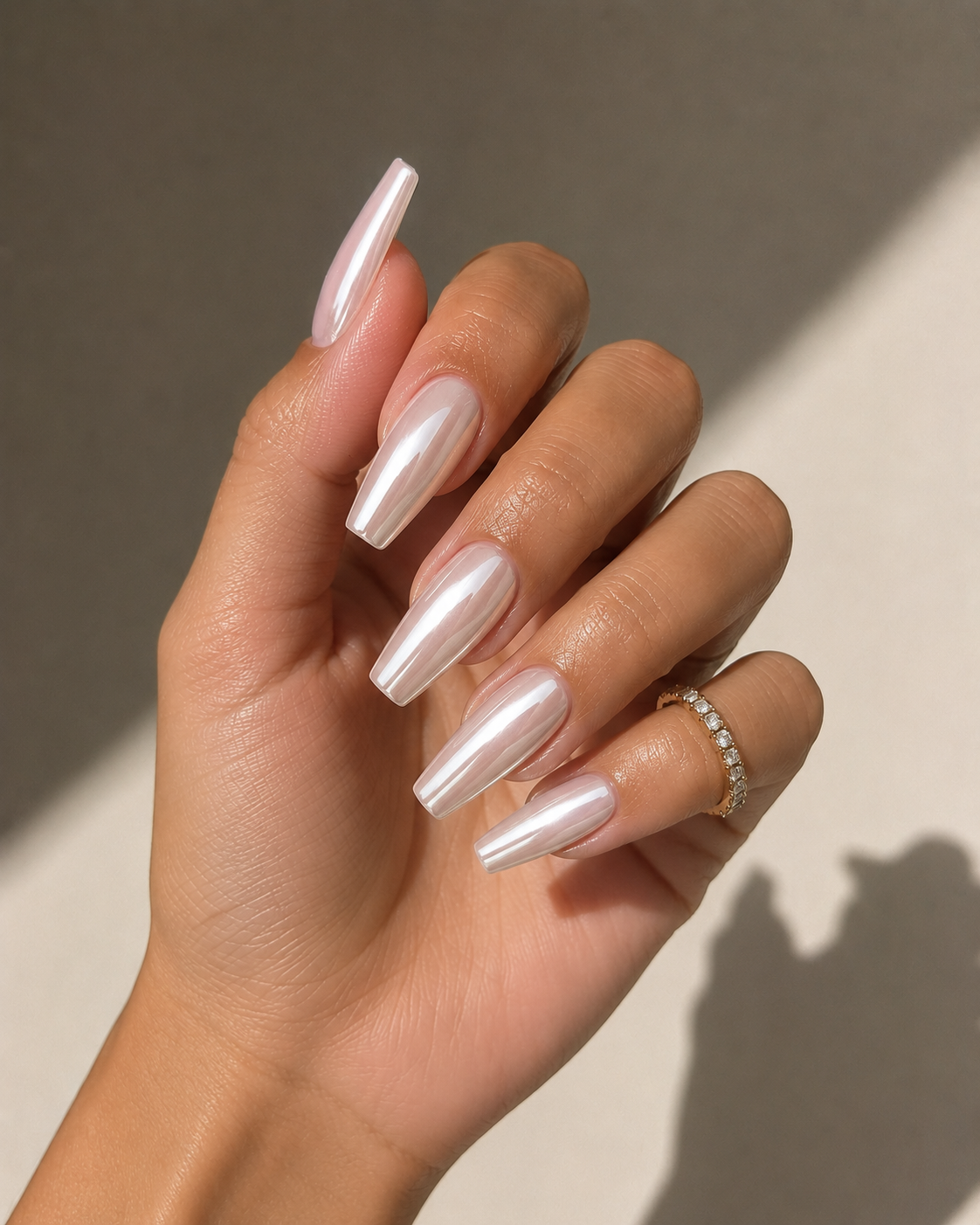 Close-up of a hand with long, coffin-shaped, glossy, light pink and white ombre nails, wearing a gold ring with small diamonds.