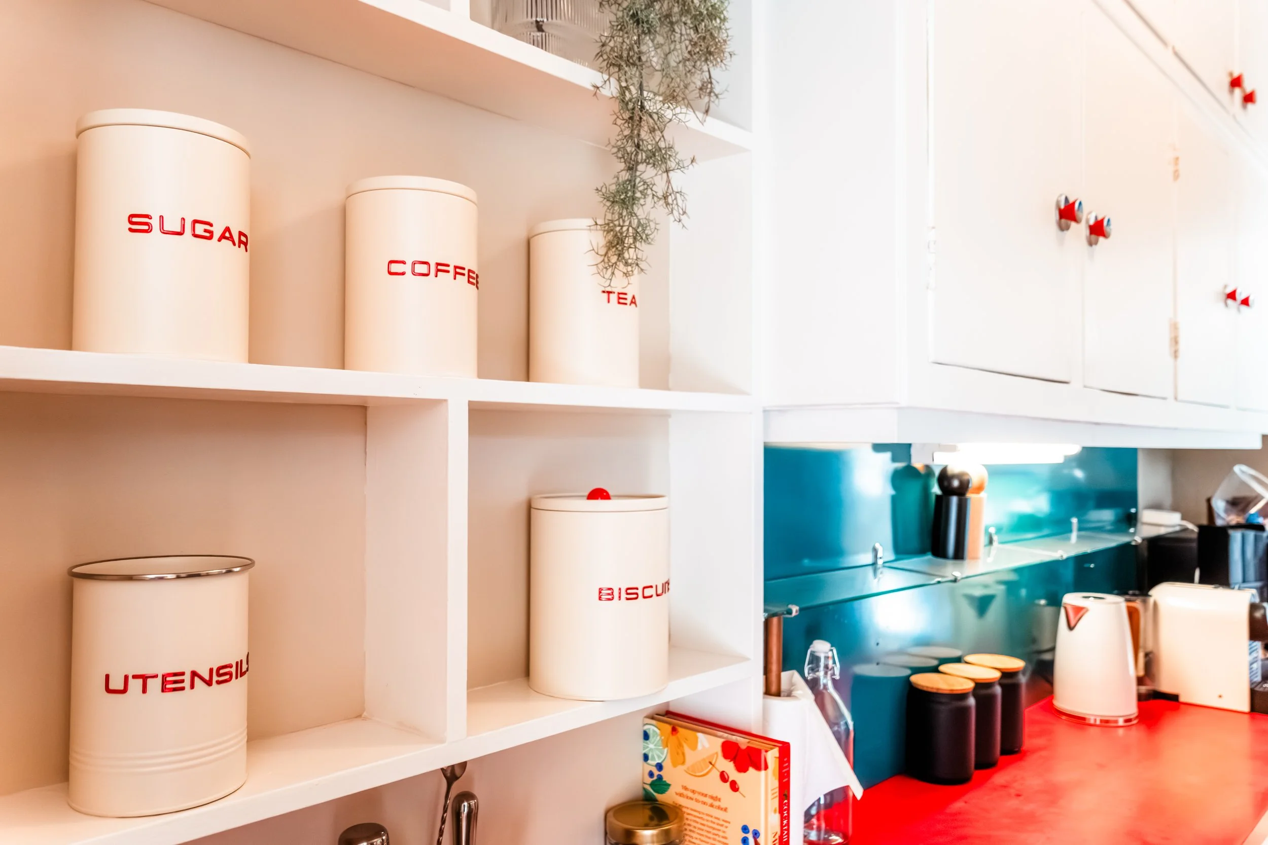 Kitchen shelf with storage canisters labeled 'sugar,' 'coffee,' and 'tea' in white containers with red text, and additional black and white containers on the counter below.