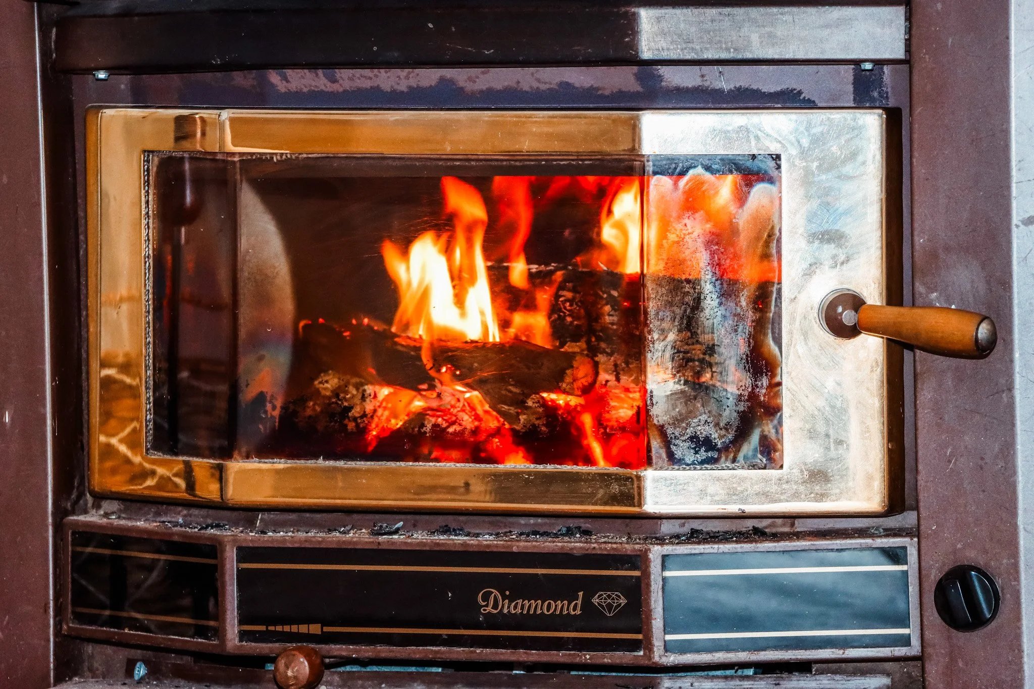 A small wood stove with a glass front, showing bright orange and yellow flames inside, with a handle on the right side.
