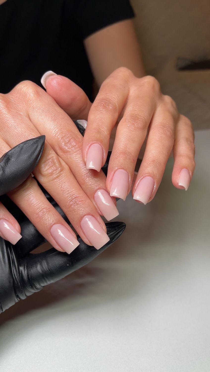 Manos con uñas acrílicas de color rosado claro en un salón de belleza.