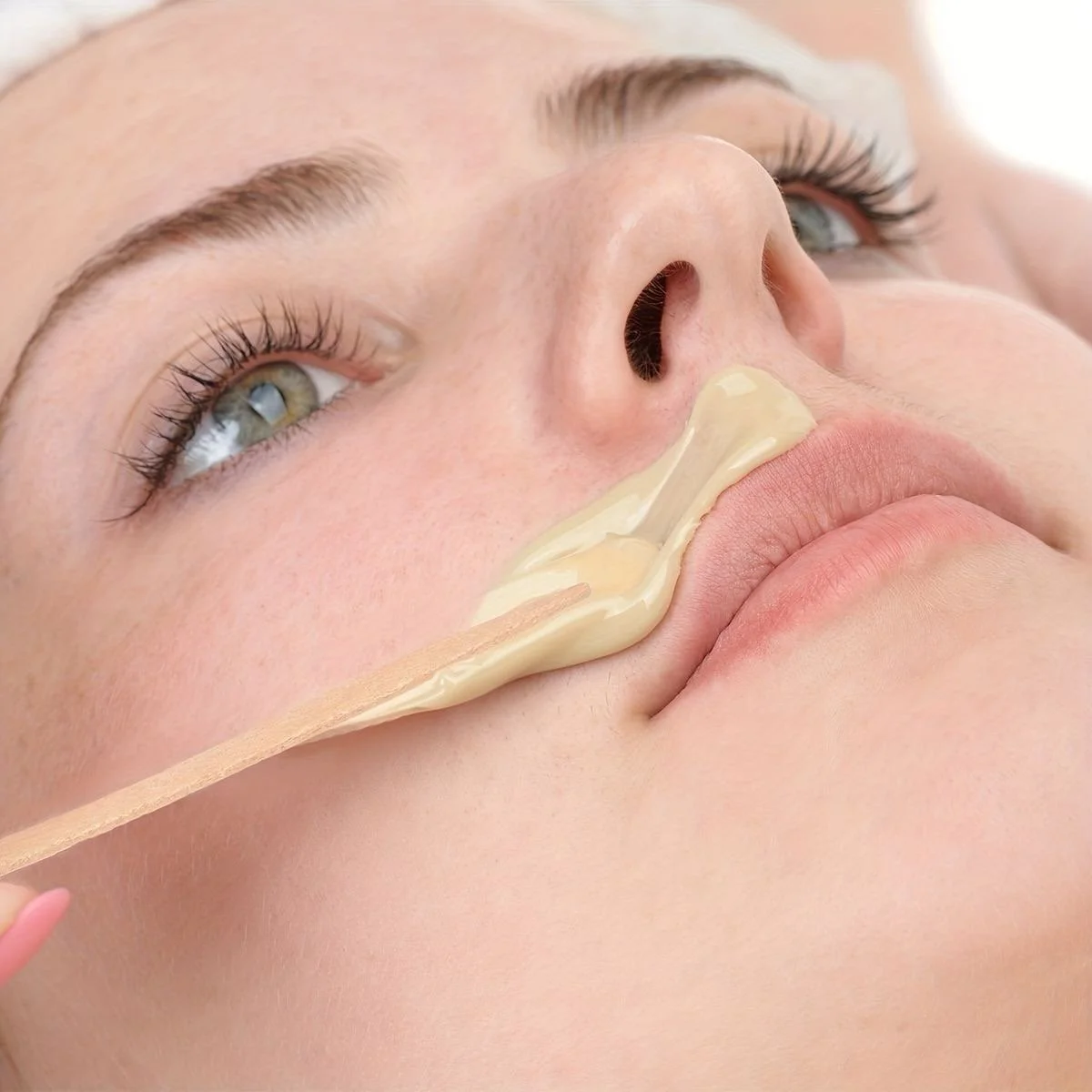 Persona aplicando cera para depilación en la zona superior del labio superior.