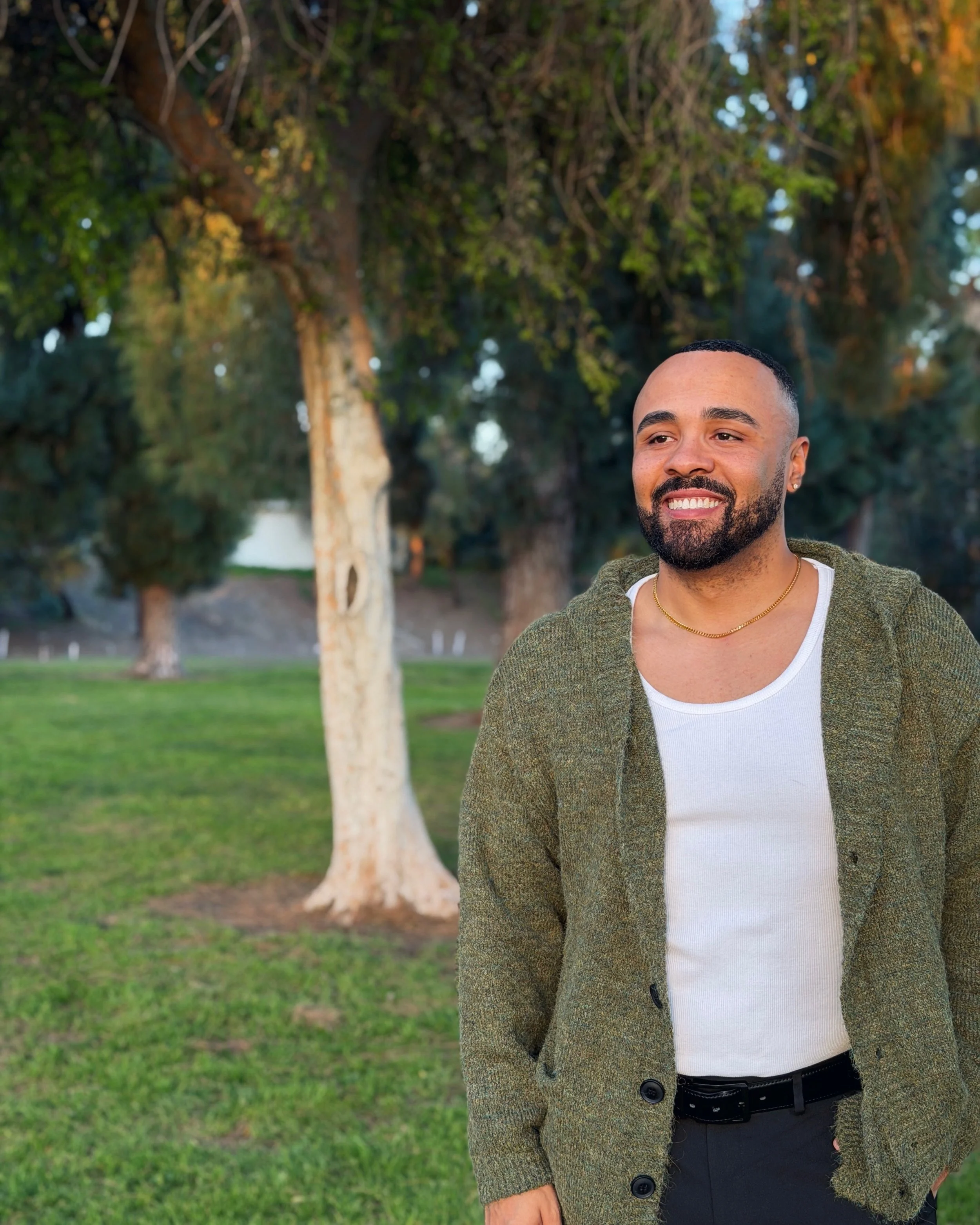 Chase Michael smiling outdoors in a park, wearing a green cardigan and white tank top