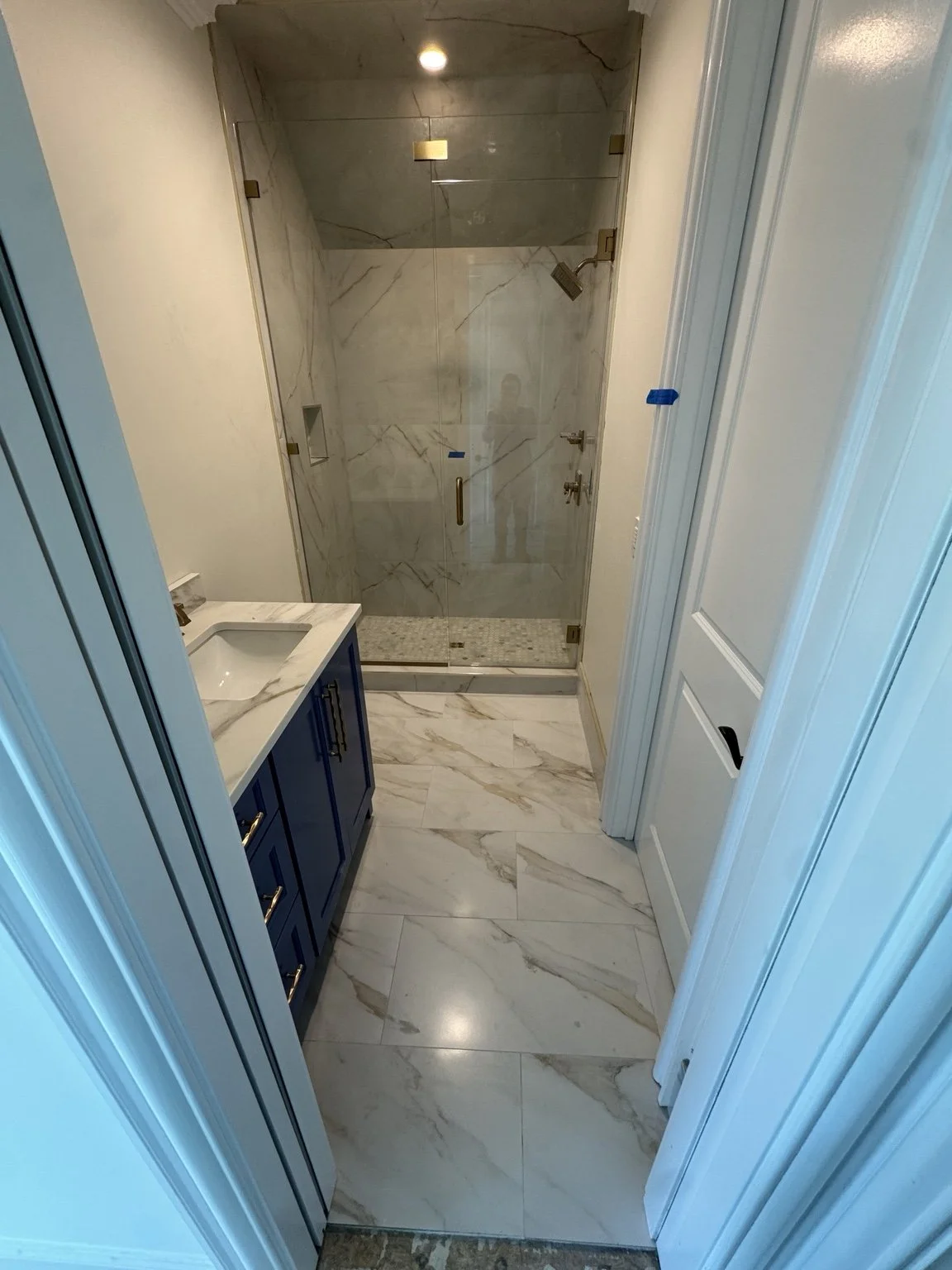Completed bathroom remodel with blue vanity, marble-look porcelain floor, and framed glass shower.