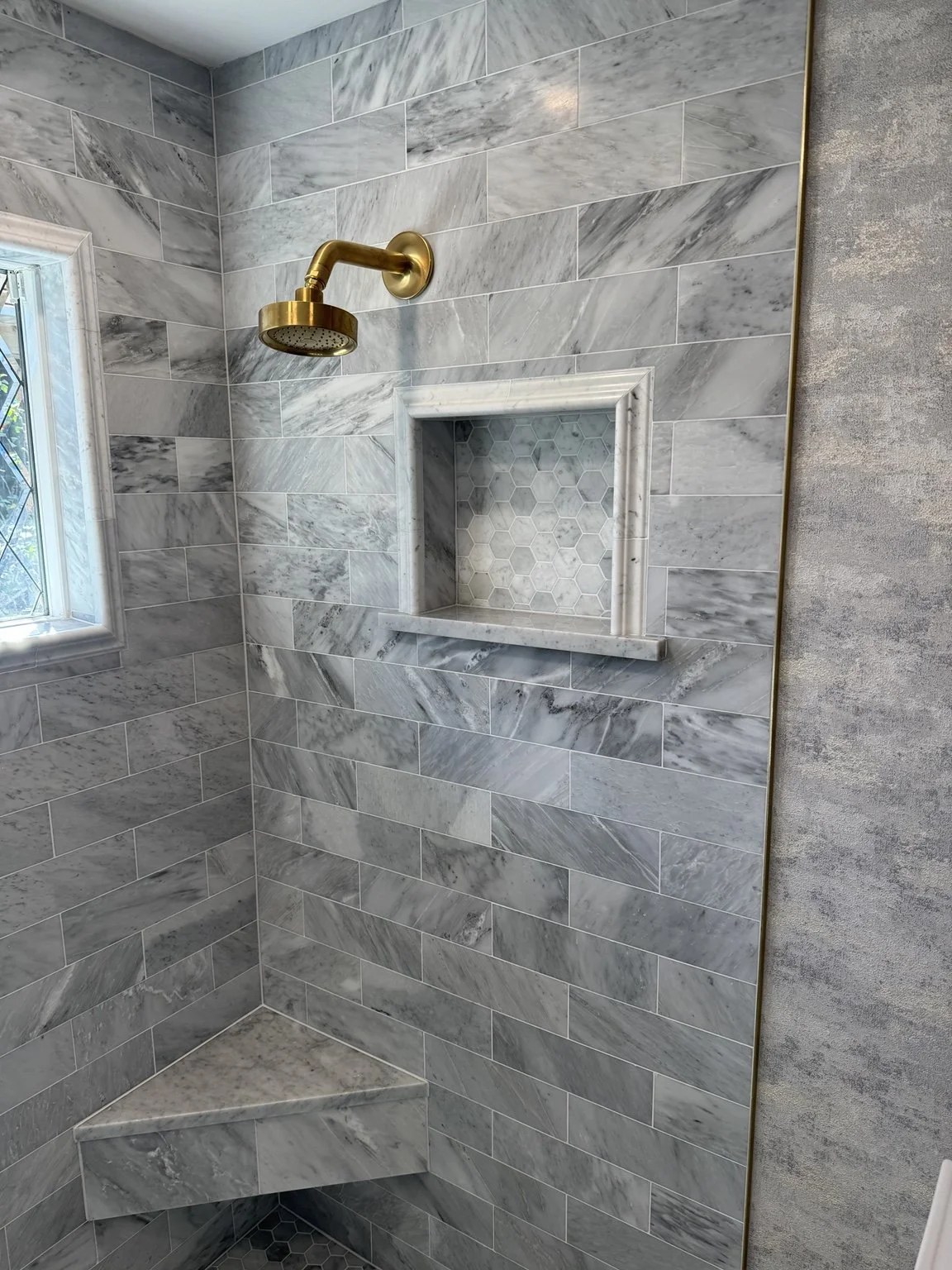 Custom marble shower detail featuring a framed niche, tiled bench, and brass shower fixture.