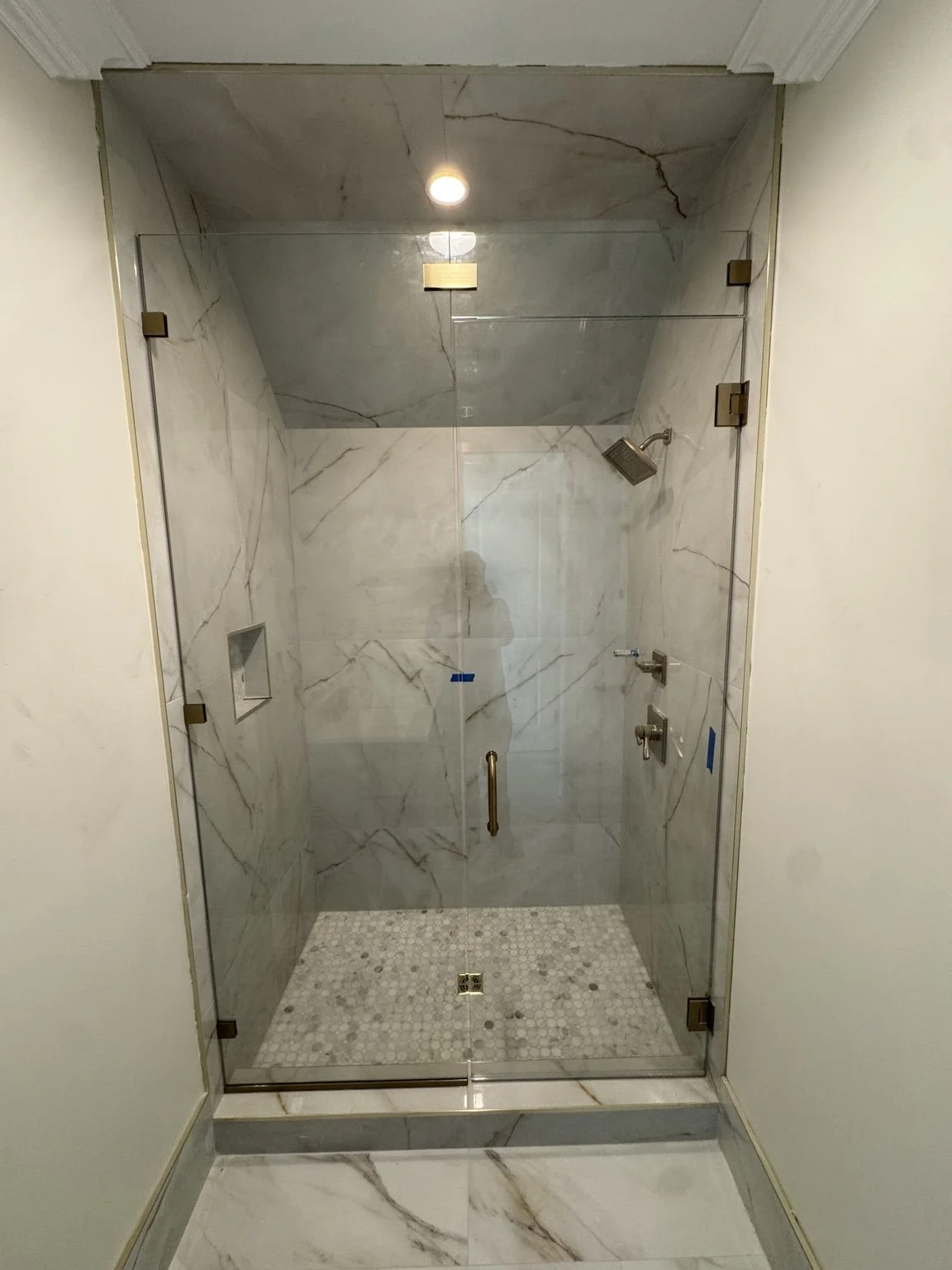 Completed XL porcelain shower with frameless glass, marble mosaic floor, and brushed-gold hardware.