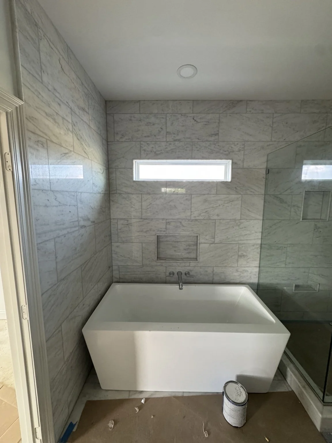 Marble-tiled bathroom with freestanding tub, wall niche, and glass shower enclosure.