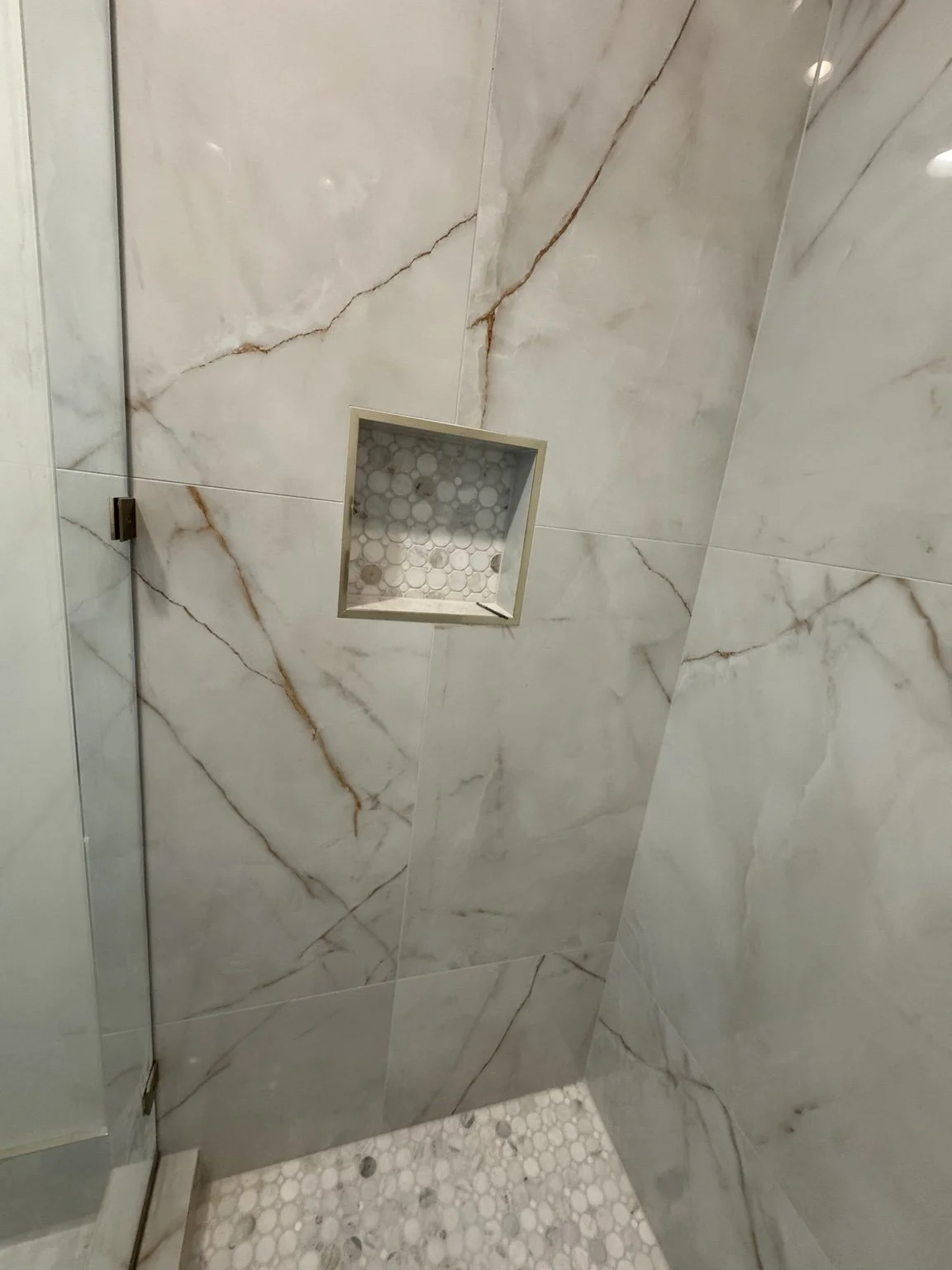 Finished large-format porcelain shower with frameless glass and a custom tiled niche.