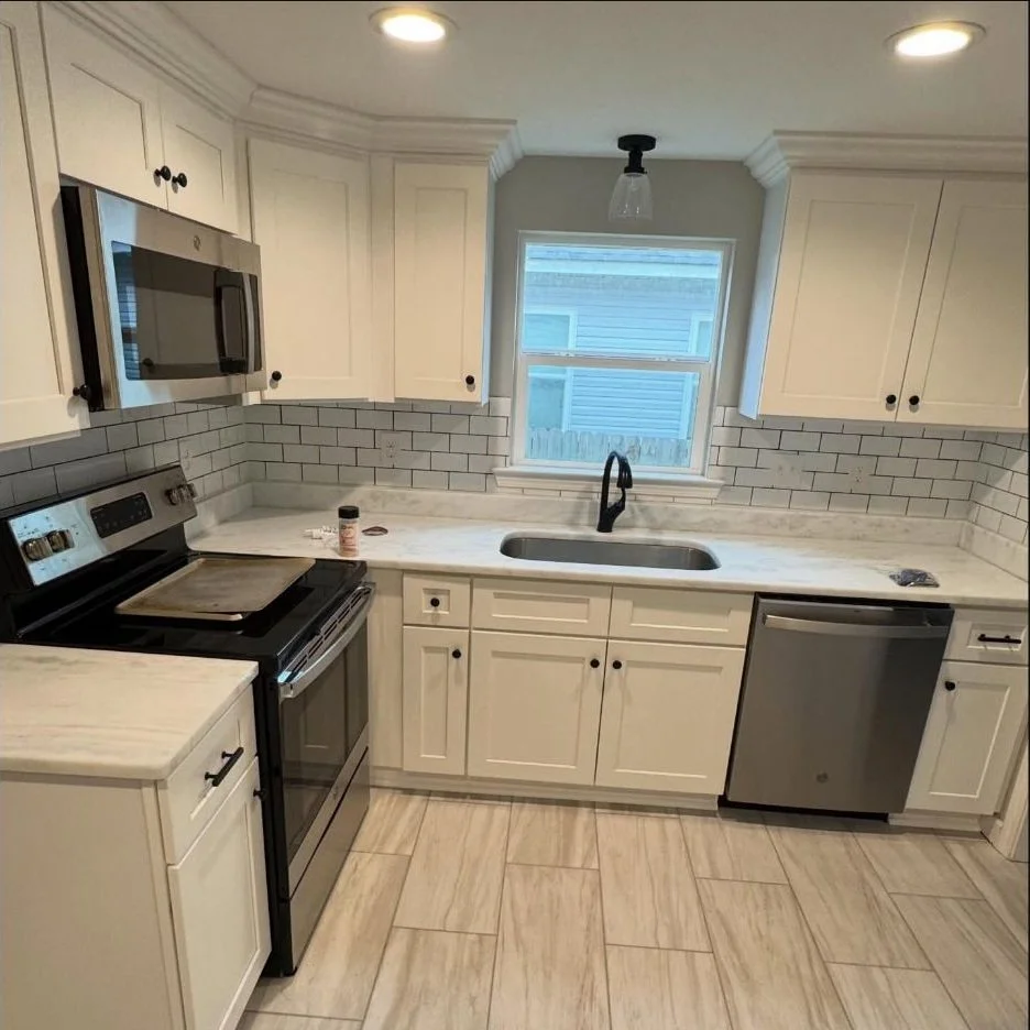 Finished white kitchen renovation with shaker cabinets, marble-look countertops, subway tile backsplash, stainless appliances, and tile flooring.