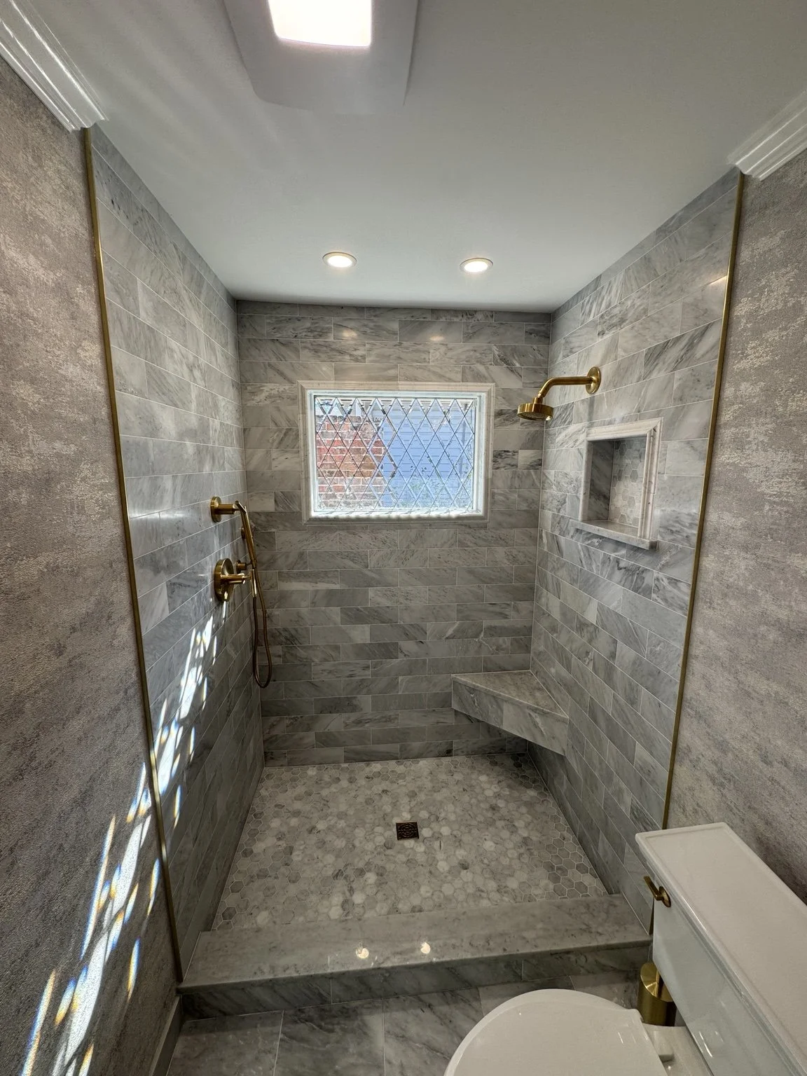 Completed gray marble walk-in shower with niche, floating bench, and brushed-gold fixtures.