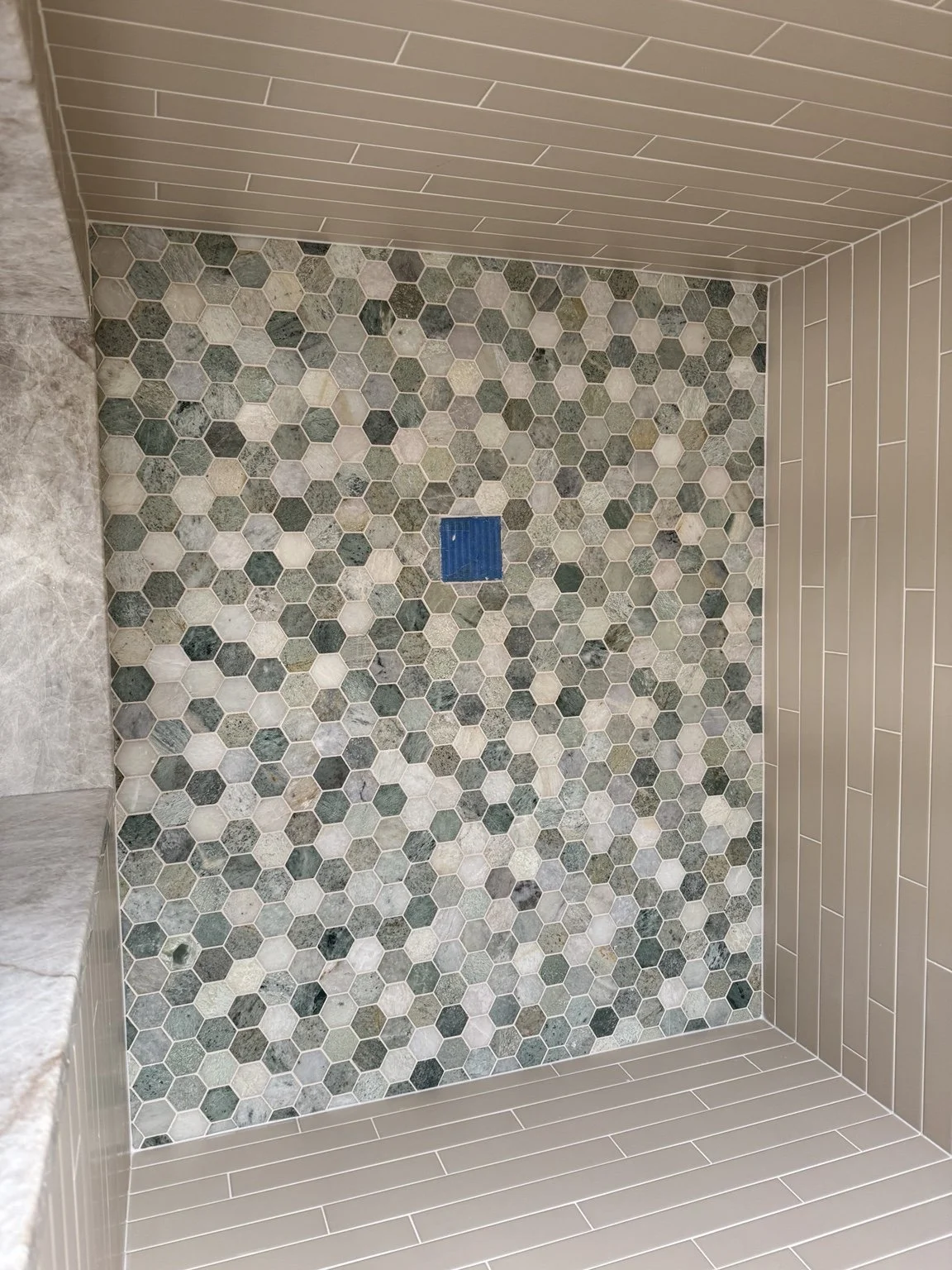 Custom shower floor with green and white hexagon mosaic tile and precisely bordered porcelain tile.