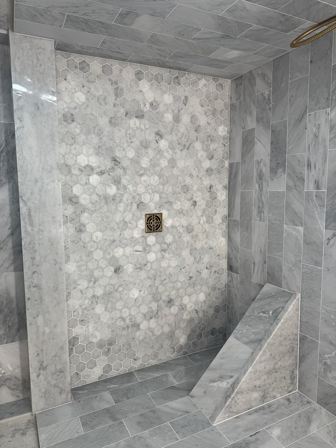 Gray marble shower floor with hexagon mosaic, custom bench, and coordinated tile walls.