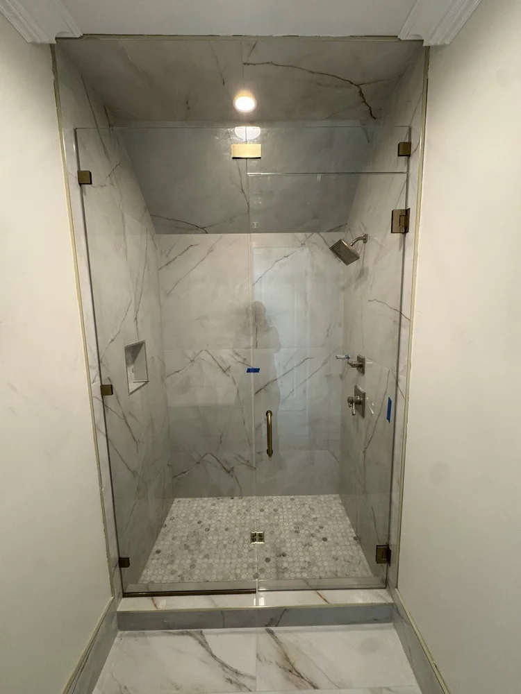 Finished large-format porcelain shower with glass enclosure, mosaic floor, recessed niche, and brass hardware.