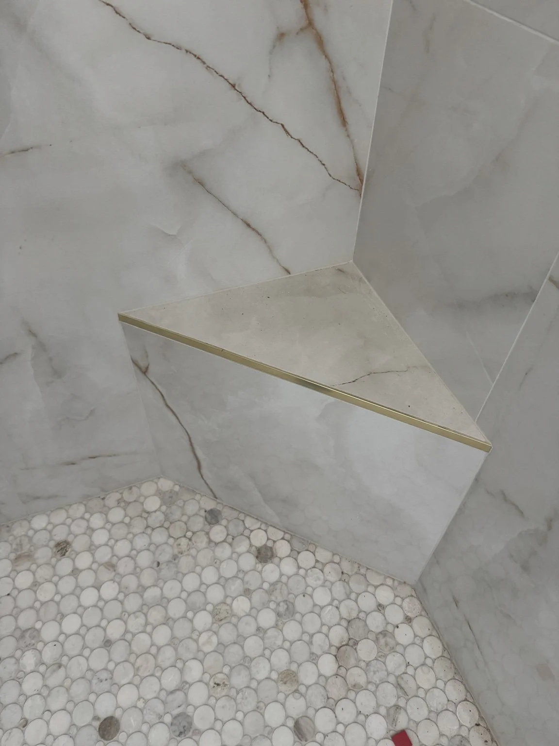 Large-format porcelain shower detail with a built-in bench and pebble mosaic floor.