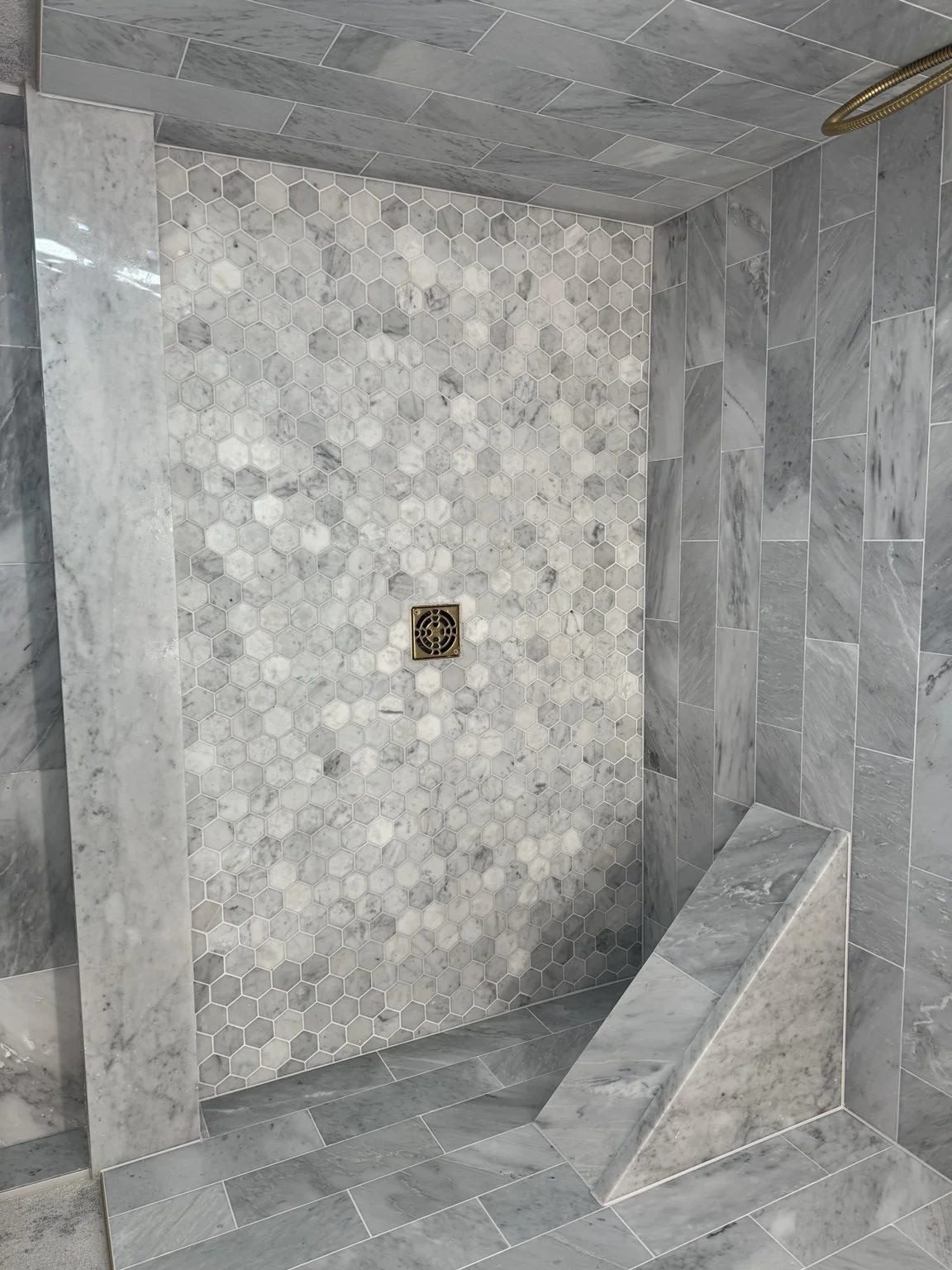 Precision-cut marble shower floor with hexagon mosaic, custom border, bench, and brass drain.