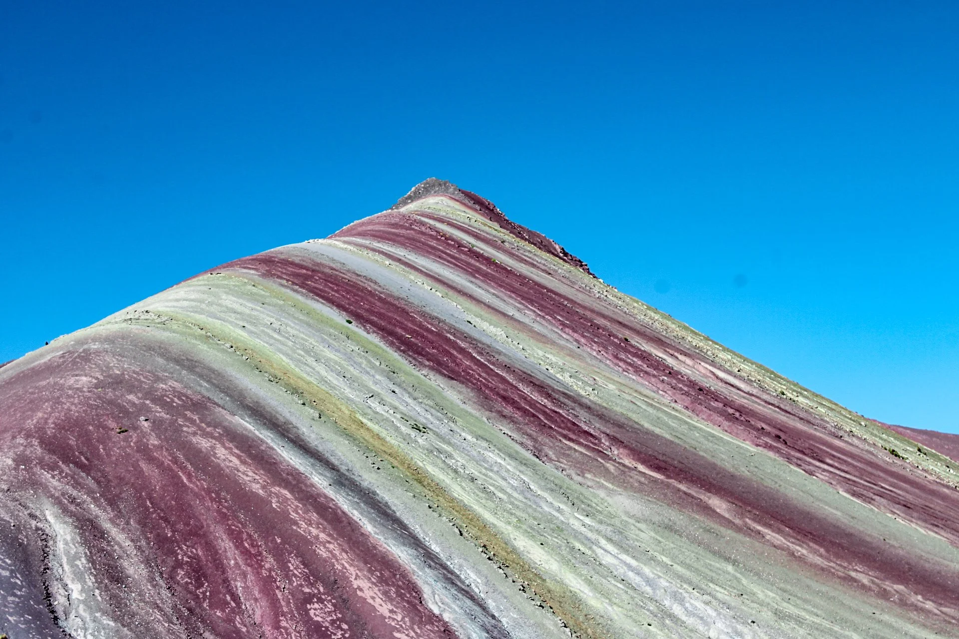 Colorful mountainous landscape with layered stripes in pink, white, yellow, and green, under a clear blue sky.