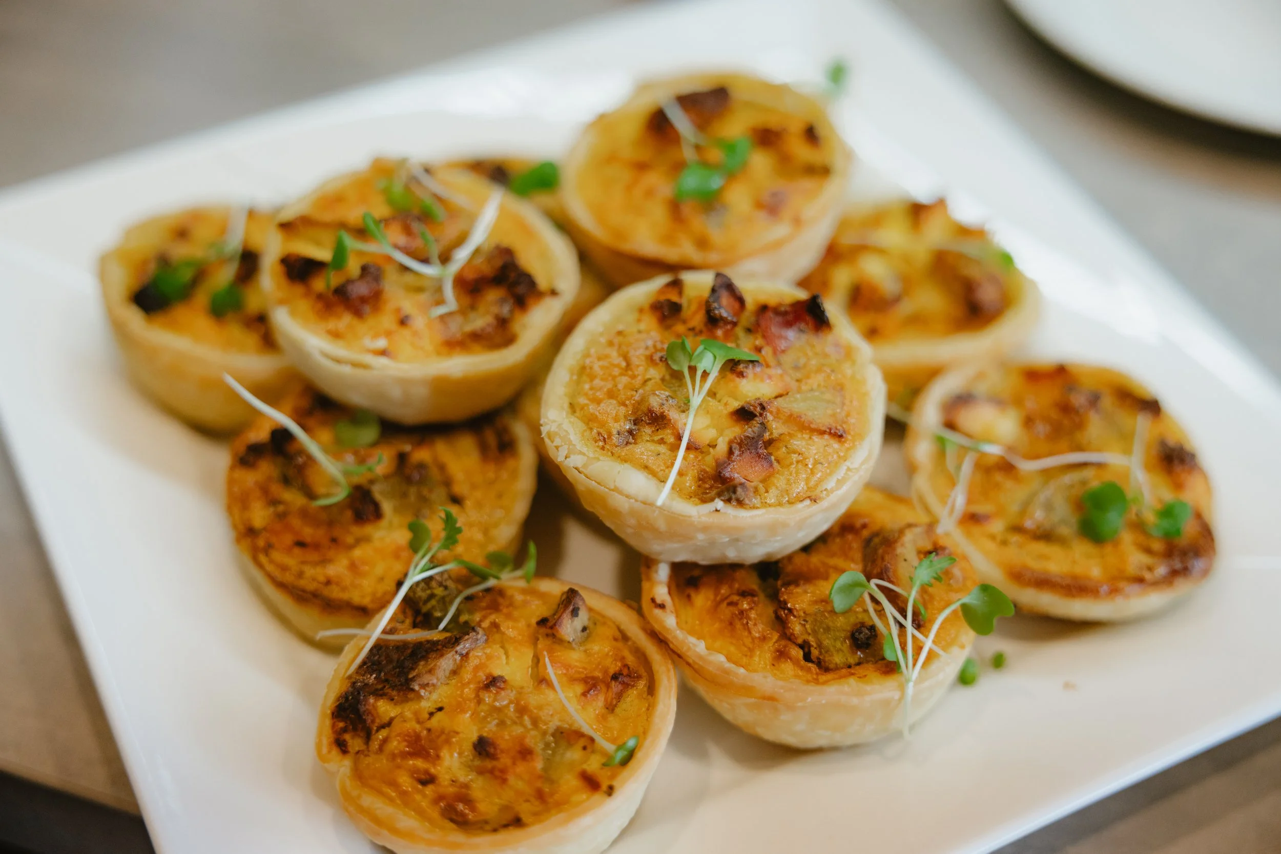 Close-up of a white platter with bite-sized, grilled, stuffed pastry cups garnished with microgreens.